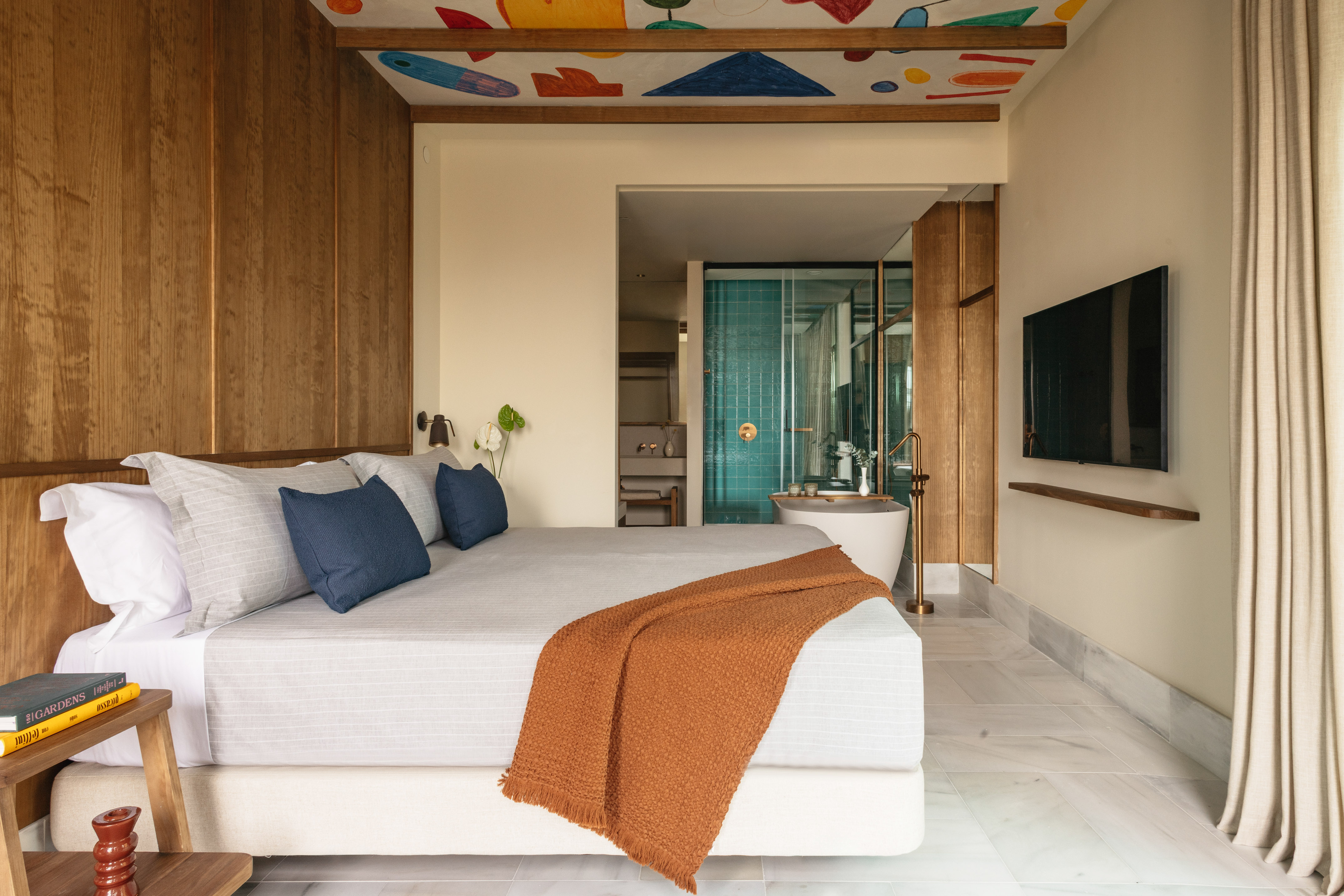 Modern bedroom with abstract ceiling art, wood paneling, and ensuite bathroom.