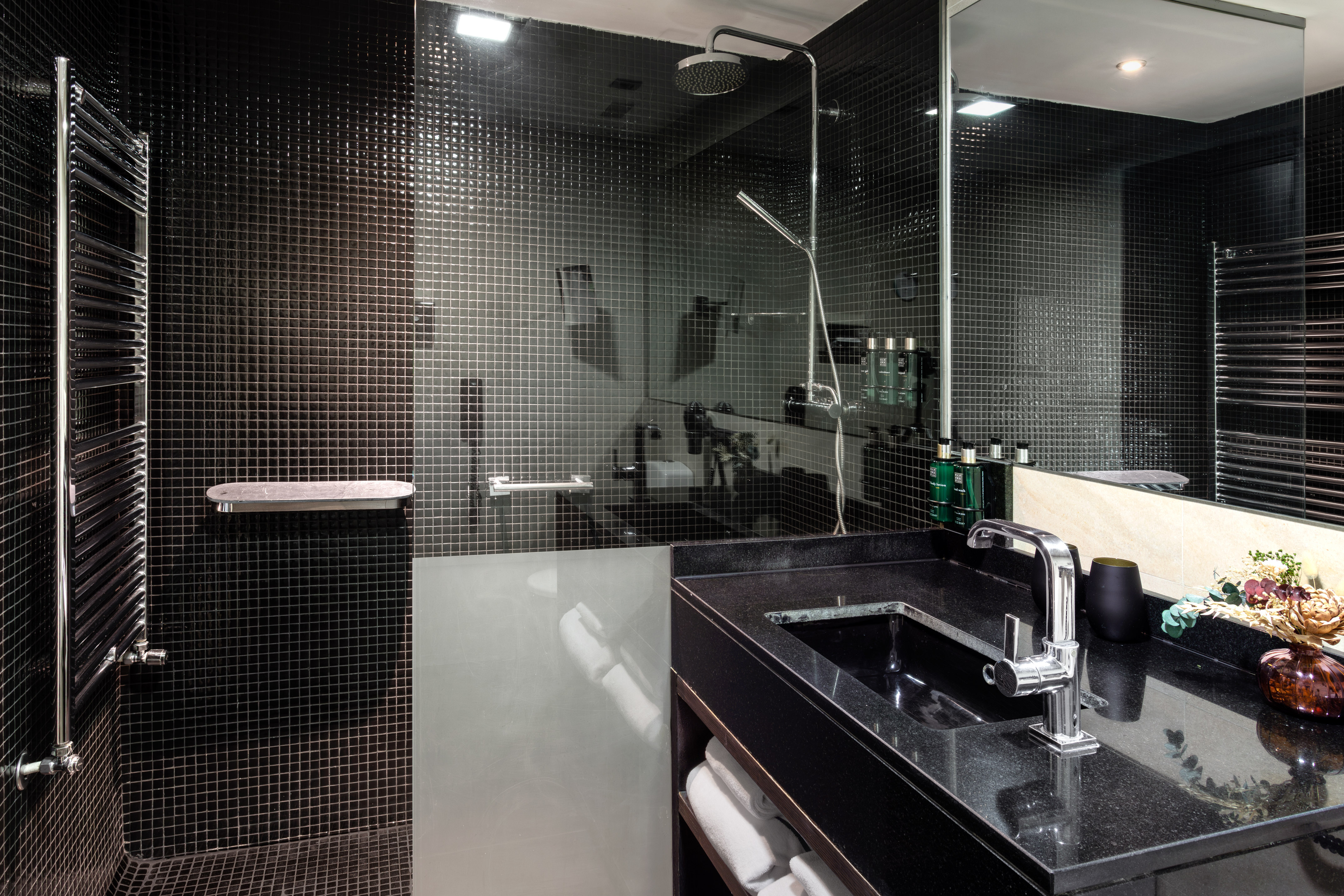 Modern bathroom with black mosaic tiles, rain shower, and black granite vanity.