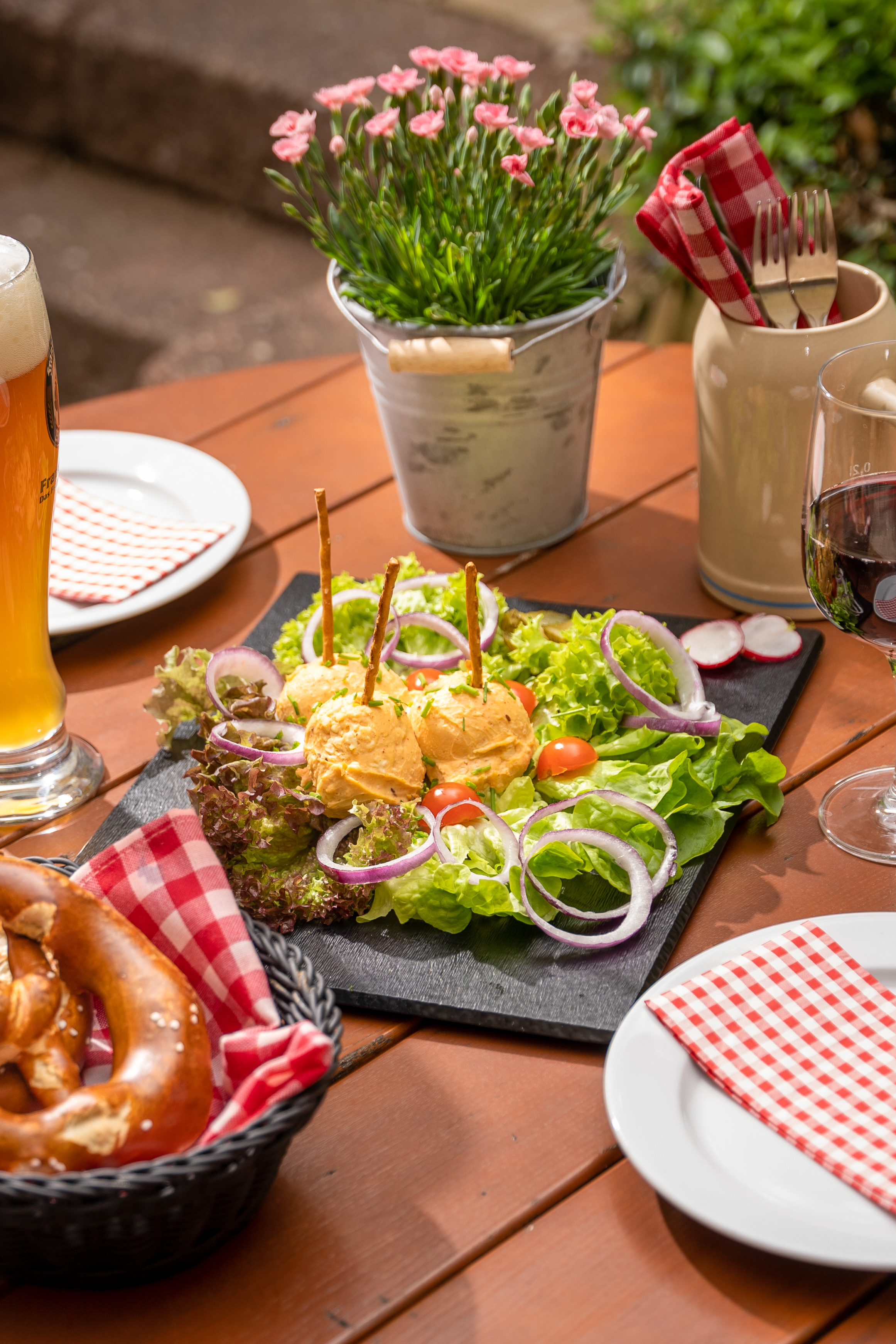 Bavarian Obatzda with fresh salad, pretzel, beer, and wine on an outdoor table.