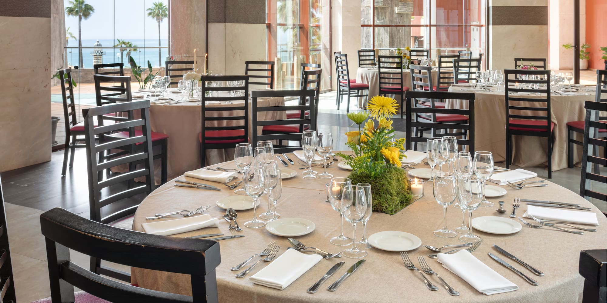 Elegant restaurant dining room with set tables, floral decor, and ocean view.