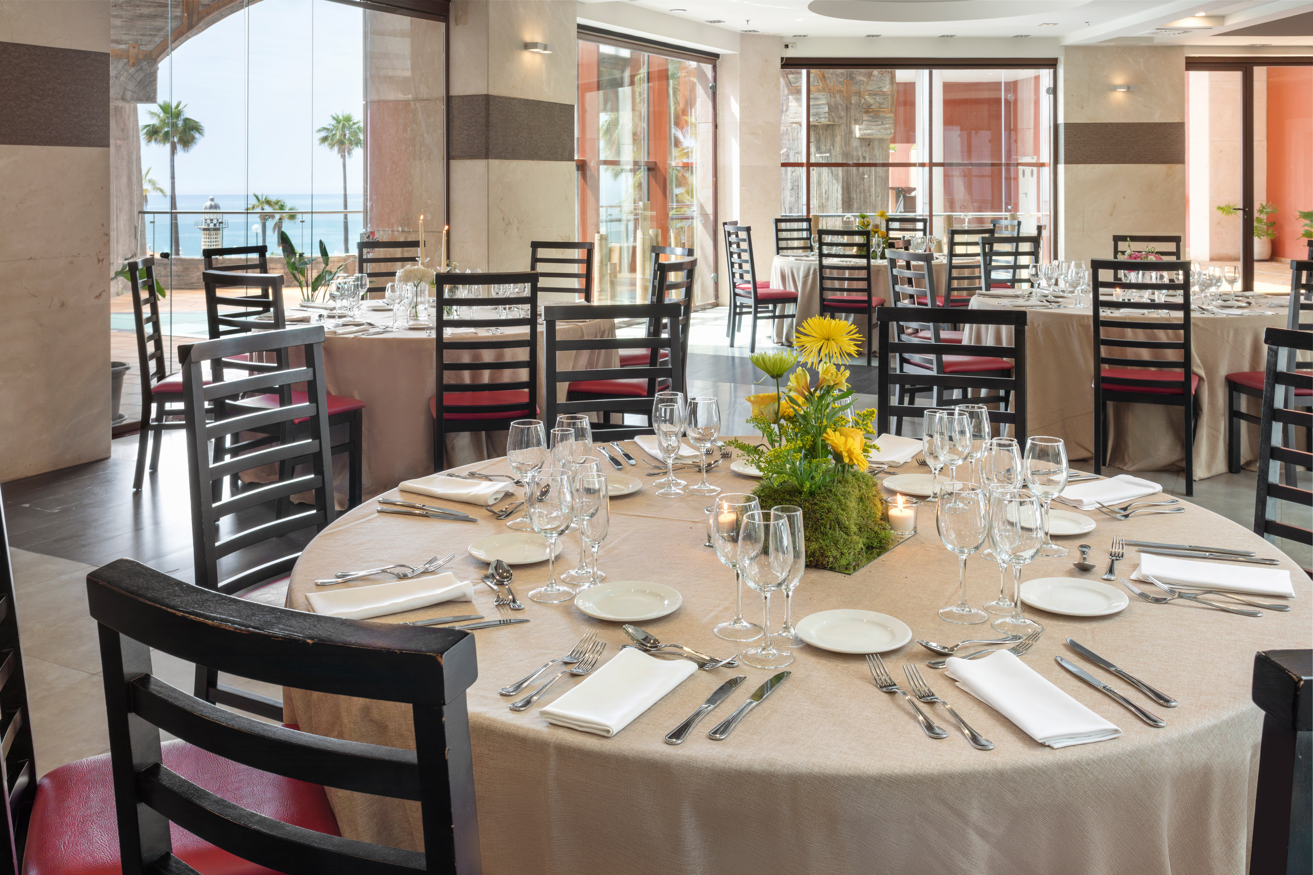 Upscale restaurant dining room with ocean view, set tables, and palm trees.