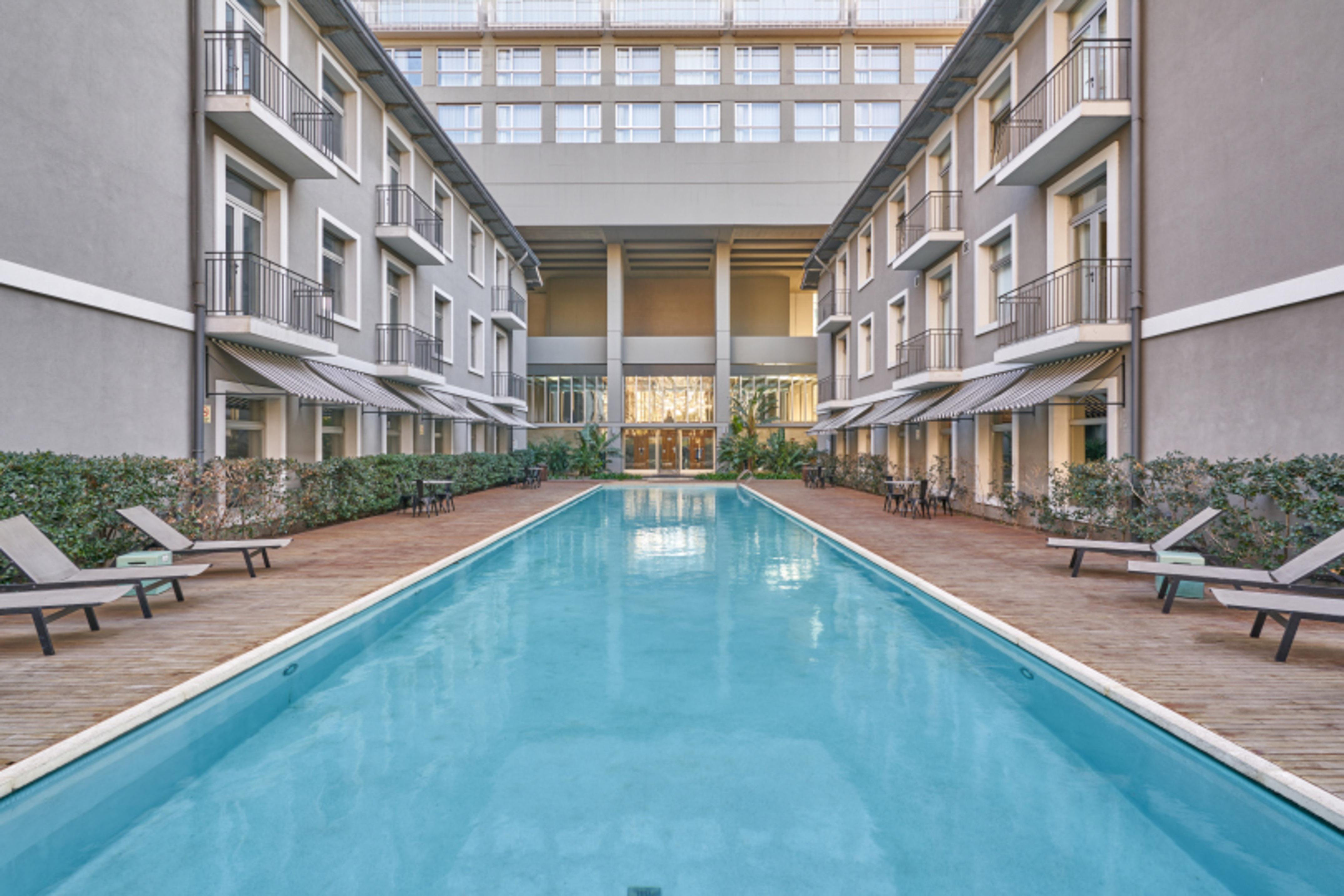 Hotel courtyard with long outdoor pool, lounge chairs, and balconies.