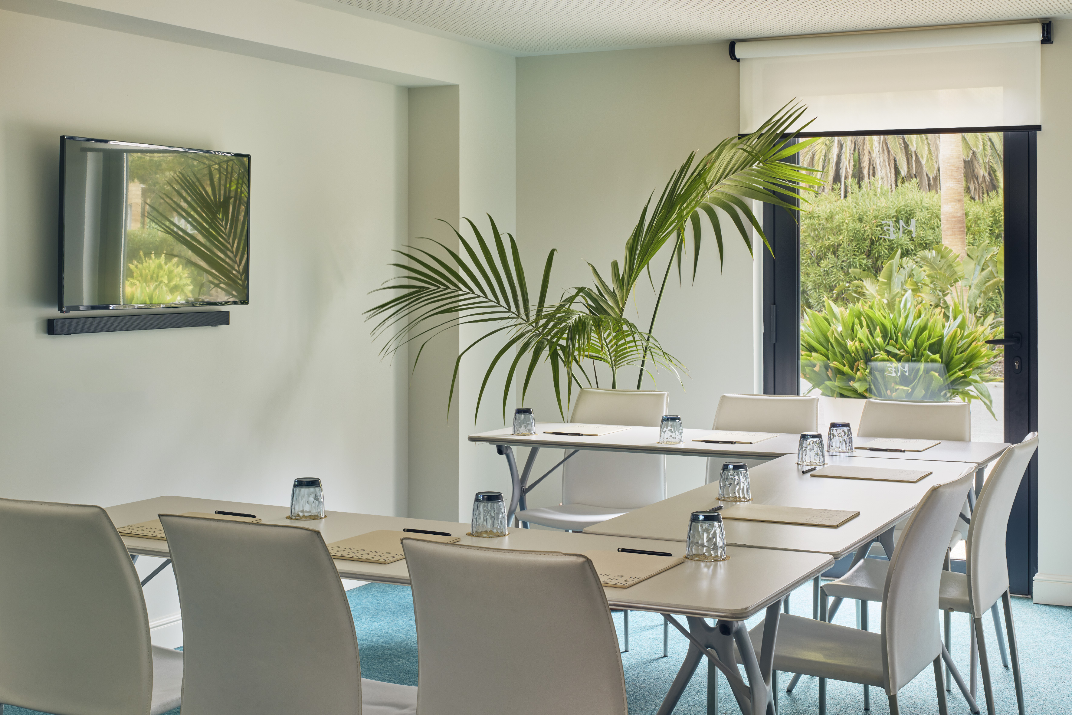 Modern U-shaped meeting room with TV, tropical plant, and garden view.