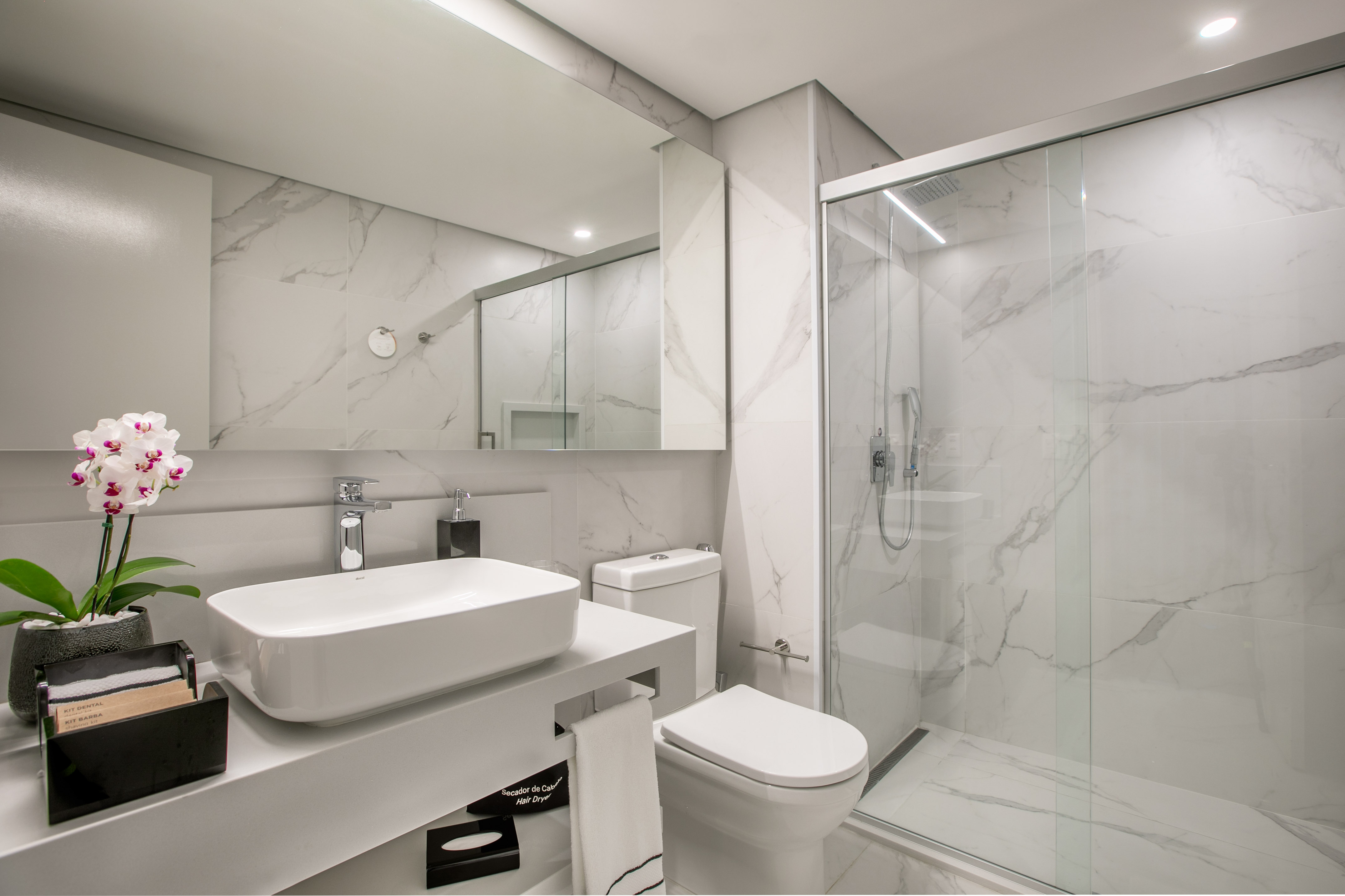 Modern white marble bathroom with glass shower, floating vanity, and orchid.