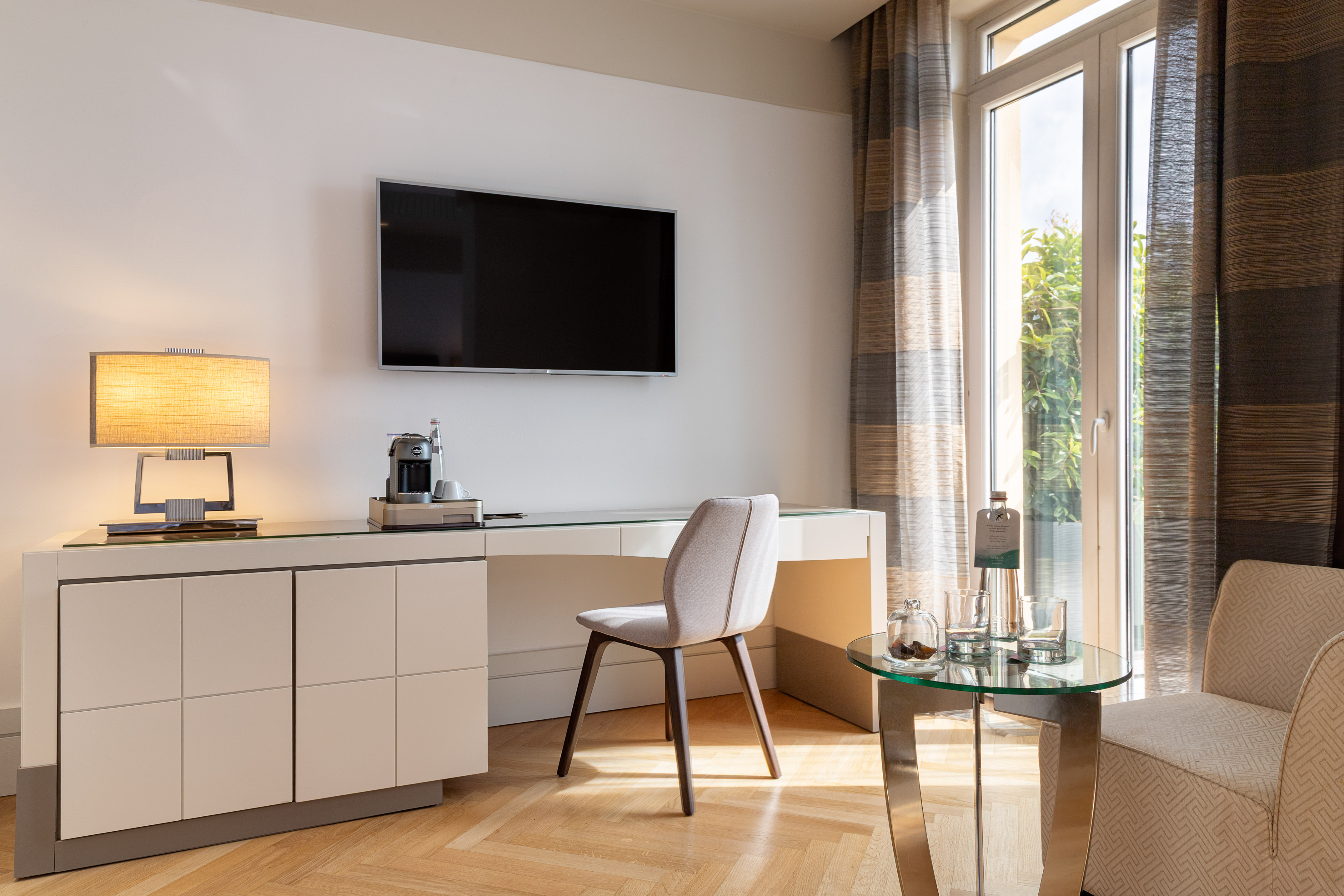 Modern hotel room desk area with TV, Nespresso machine, and bright window.