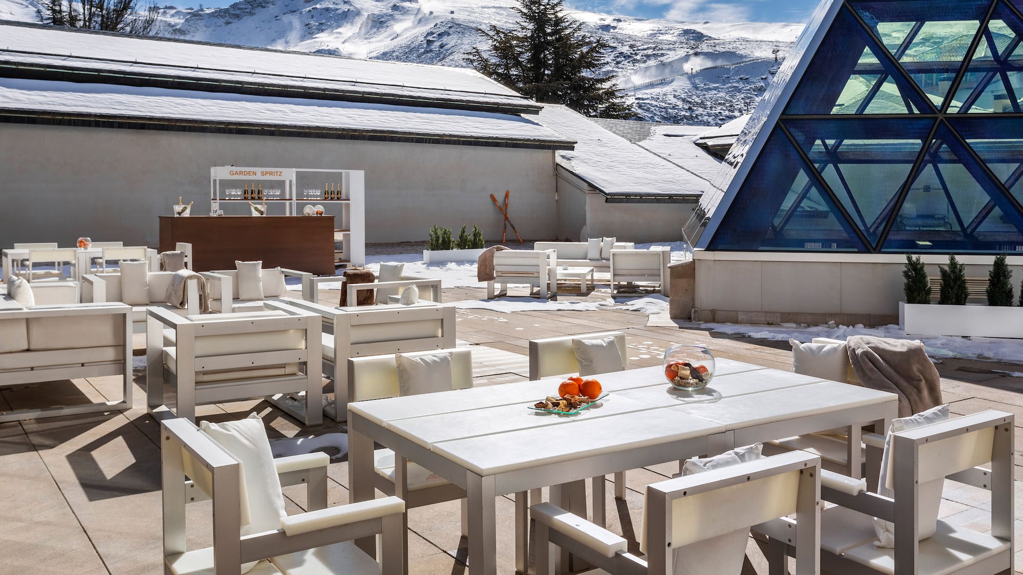 a white tables and chairs outside with snow covered mountains in the background