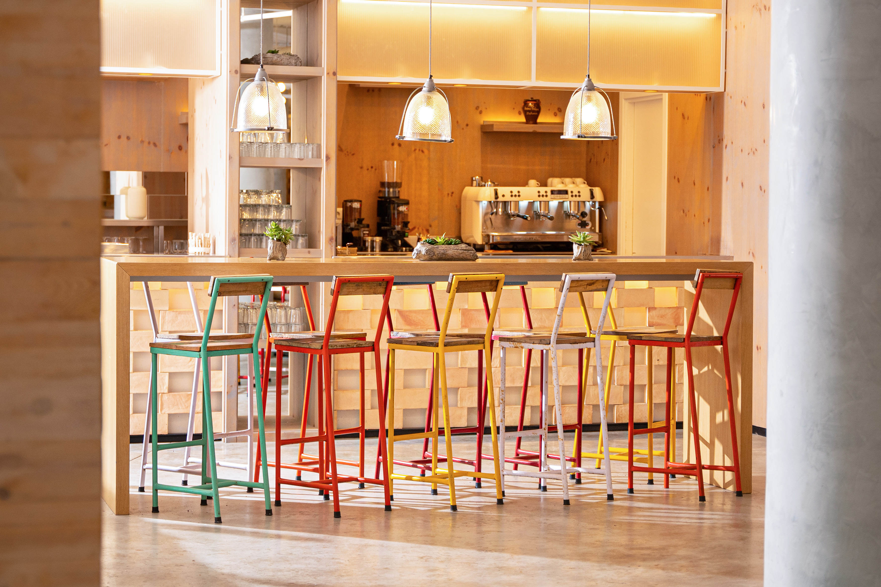 Vibrant bar stools at a modern wooden coffee bar with espresso machine.