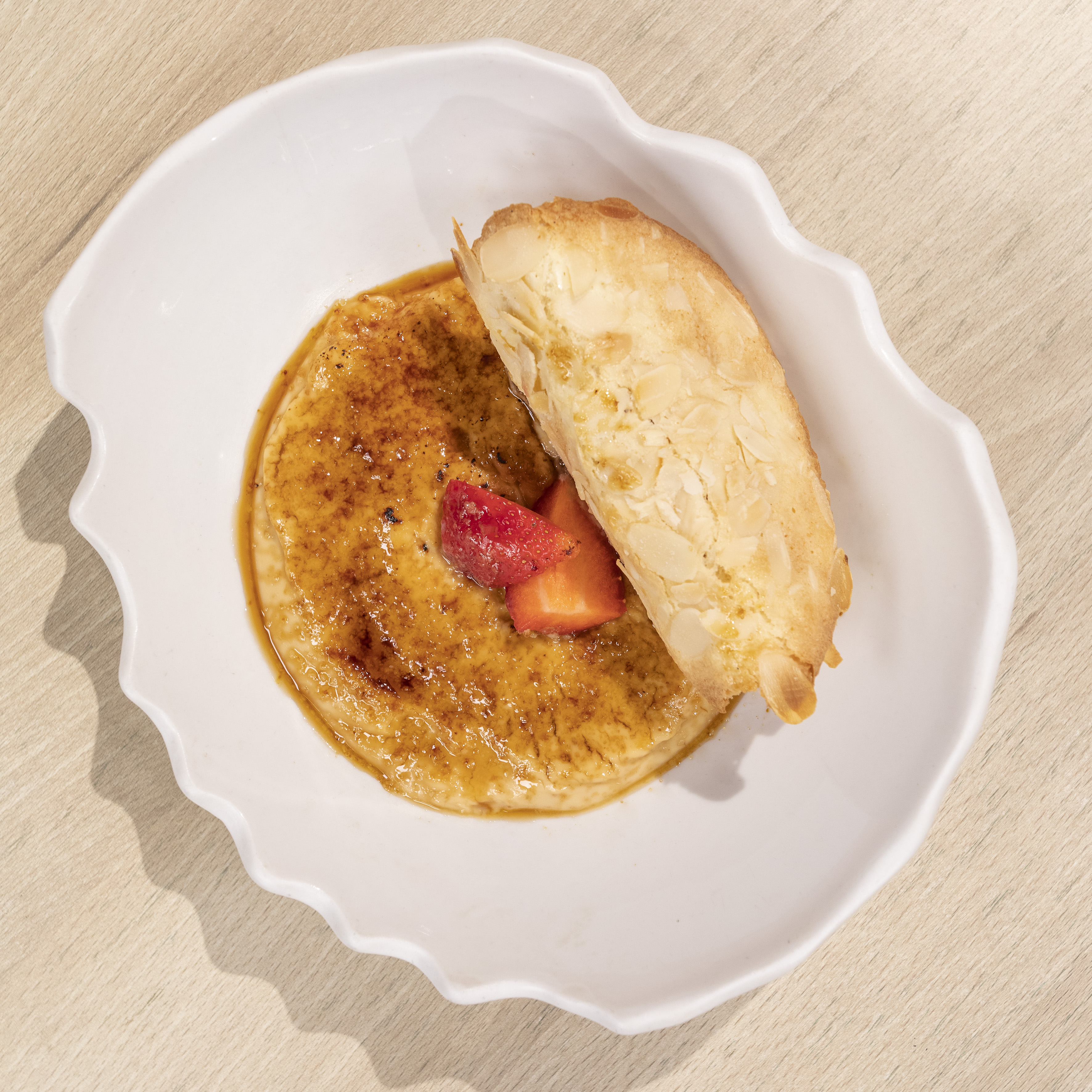 Crème brûlée with caramelized topping, sliced strawberries, and almond tuile.