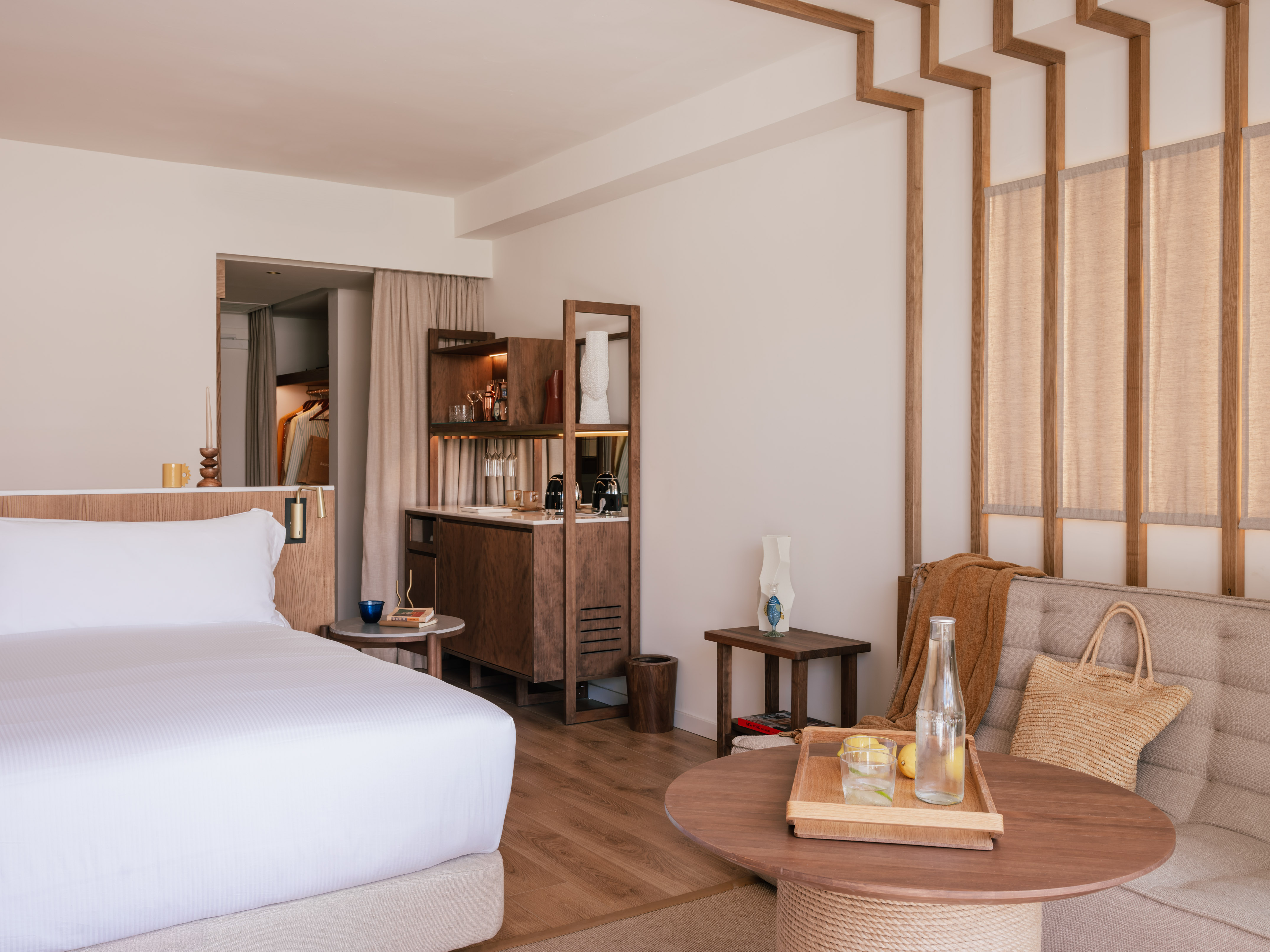 Luxury hotel suite: modern bedroom, white bed, wooden mini-bar, seating.