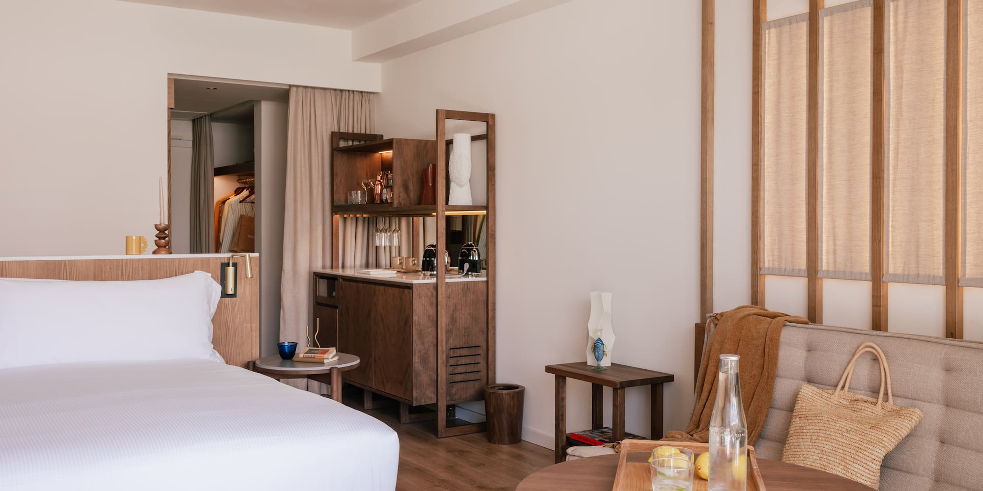 Luxury hotel suite: modern bedroom, white bed, wooden mini-bar, seating.