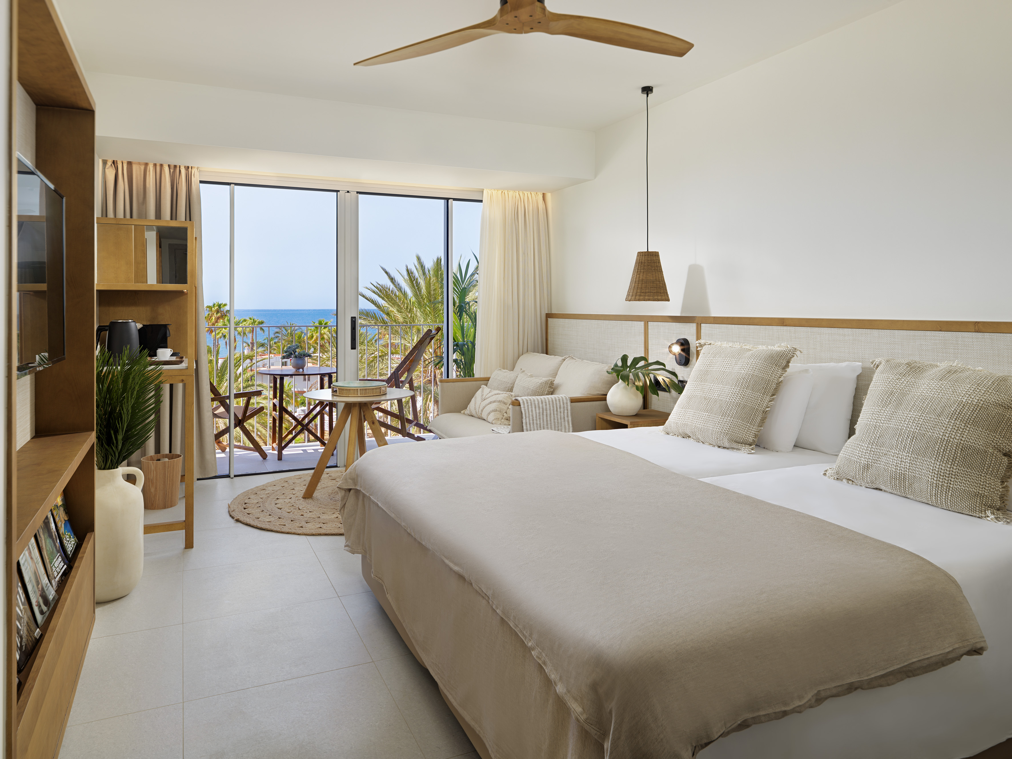 Bright hotel bedroom with ocean view balcony, bed, and tropical decor.