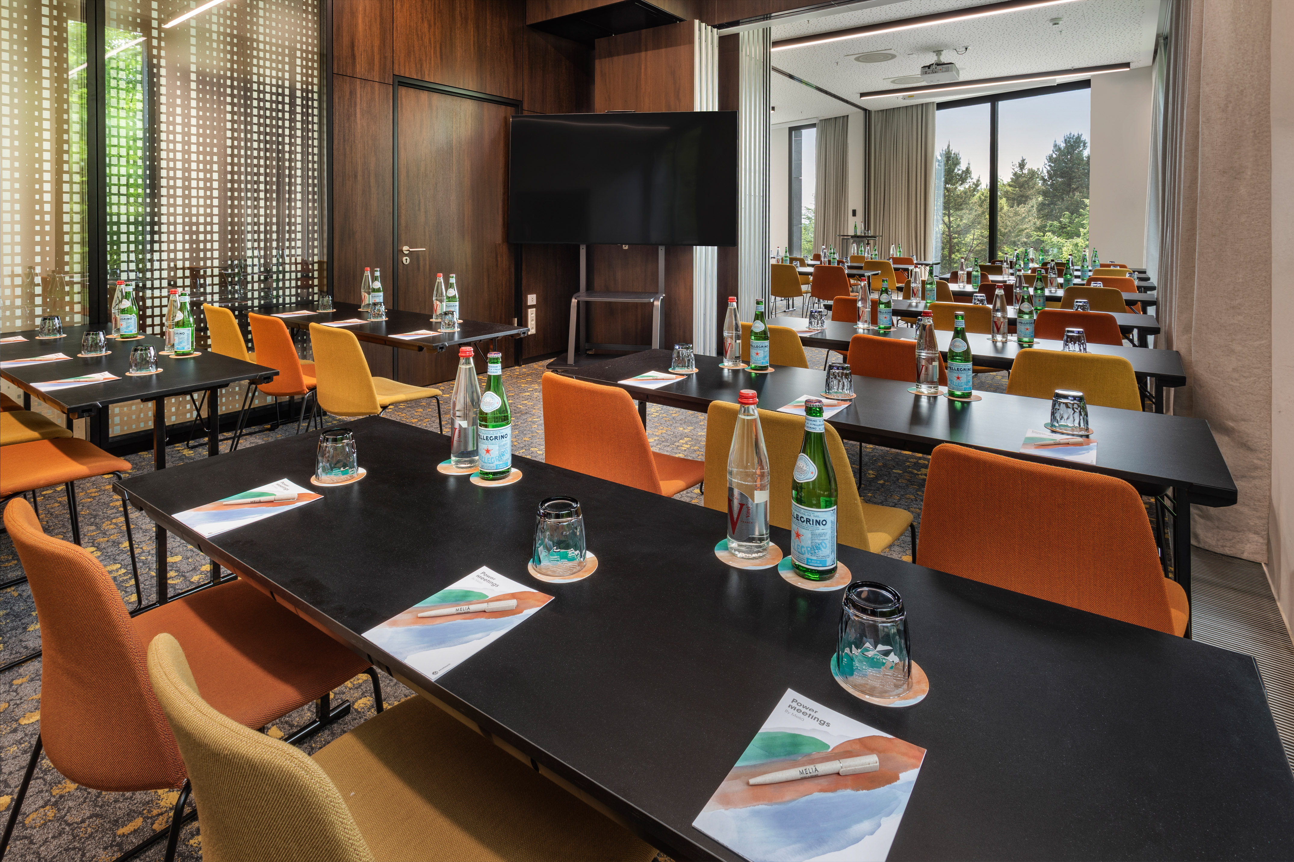 Modern meeting room with black tables, colorful chairs, presentation screen.