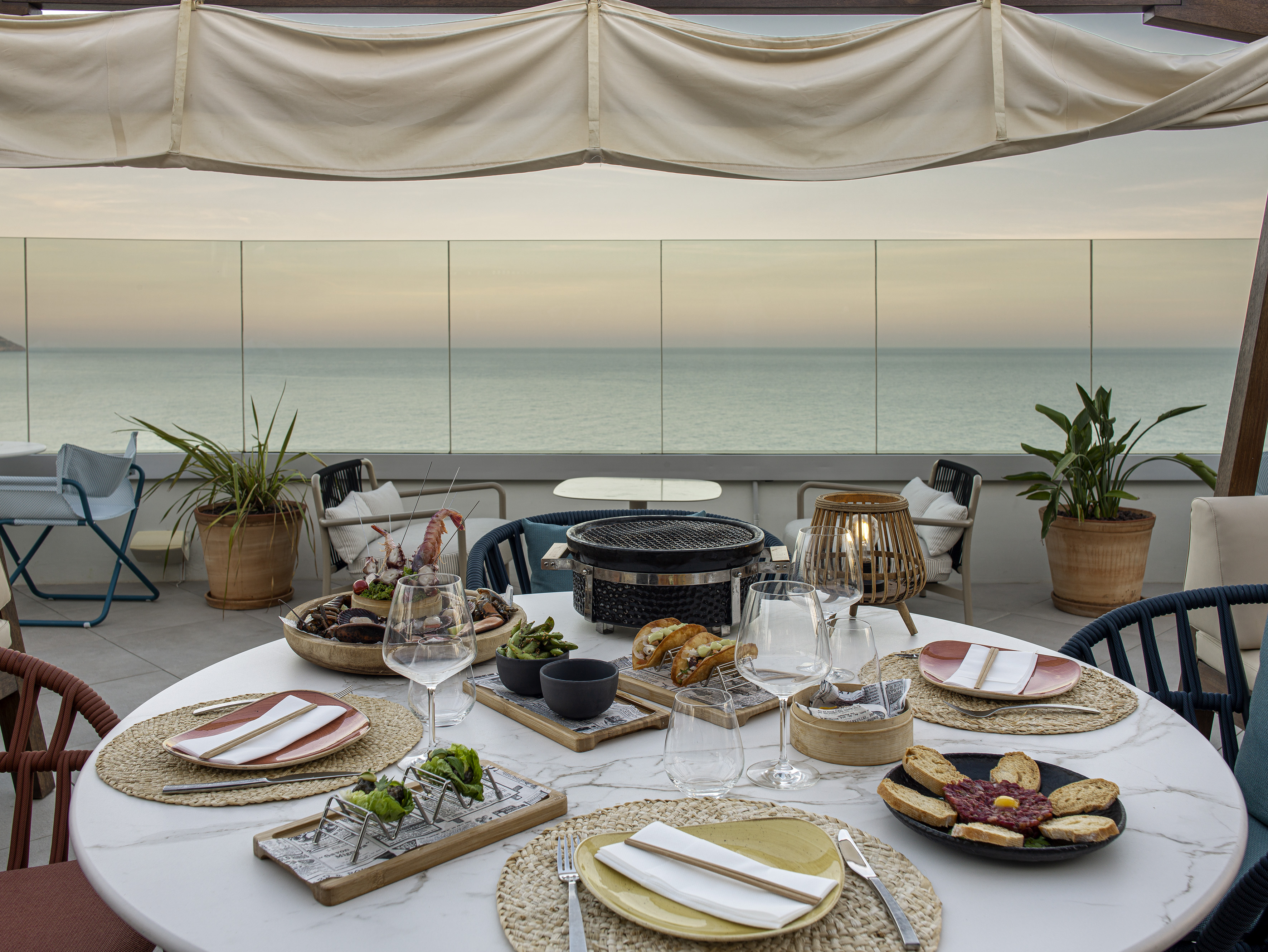 Oceanfront rooftop dining with seafood, portable grill, and sunset view.