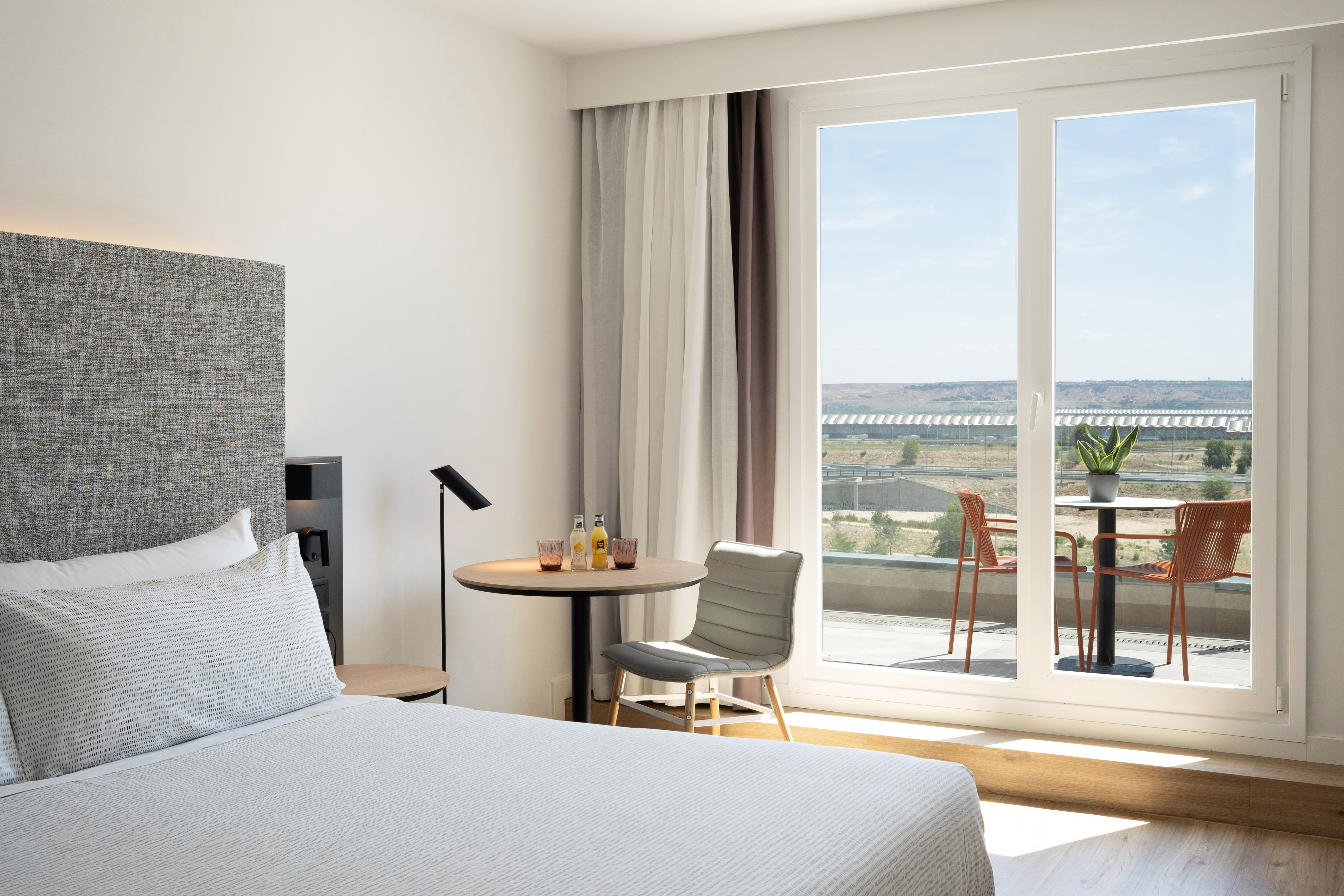 Modern hotel room, bed, and balcony overlooking a scenic landscape.