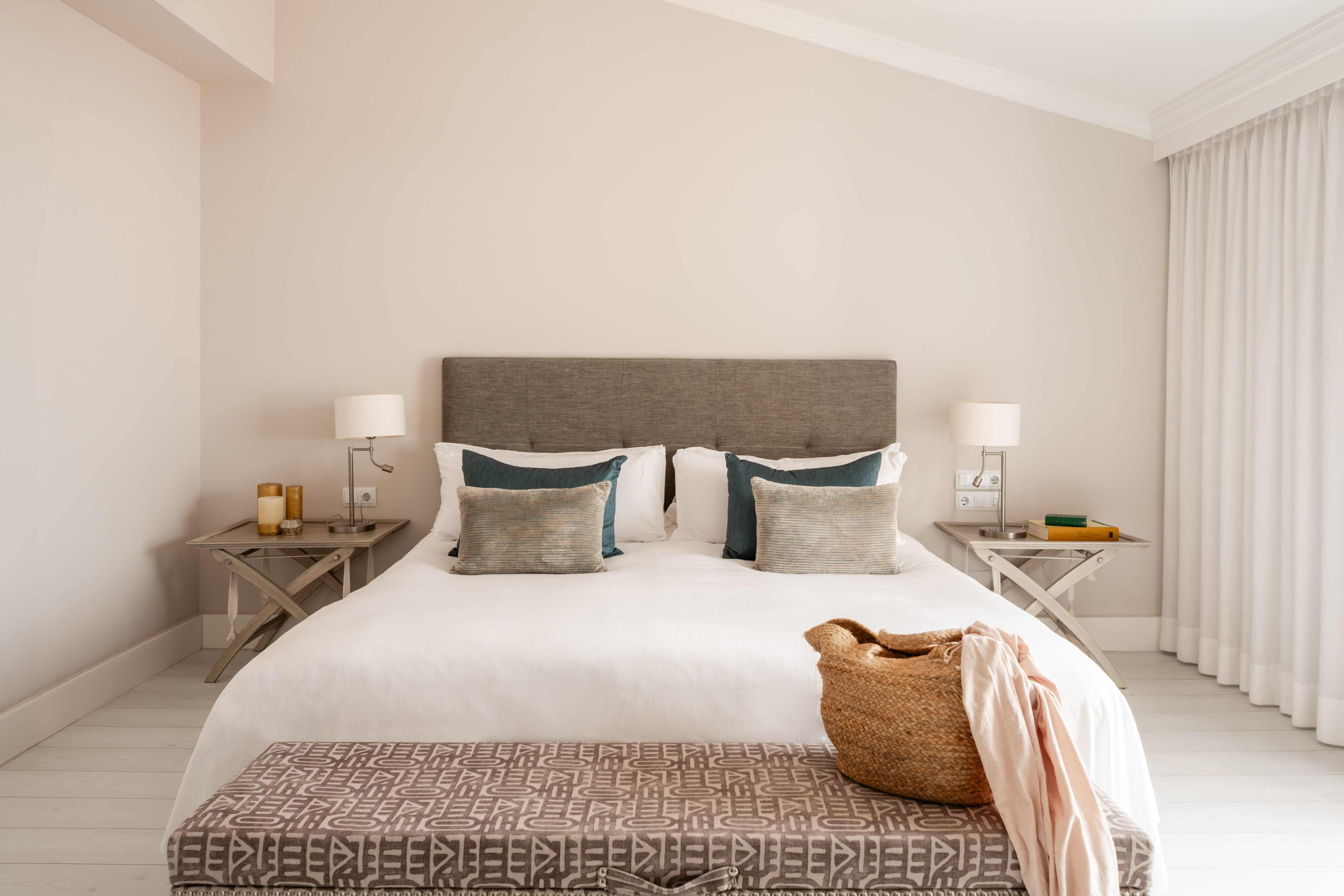 Neutral bedroom with upholstered bed, white bedding, and patterned bench.