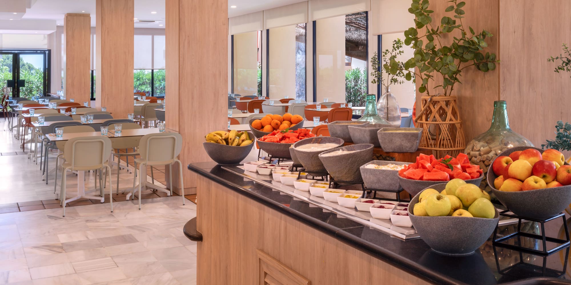 Hotel restaurant breakfast buffet with fresh fruit and dining tables.