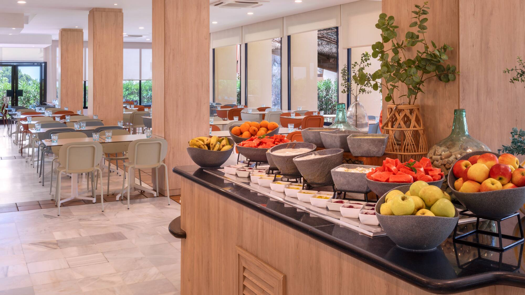 Hotel restaurant breakfast buffet with fresh fruit and dining tables.