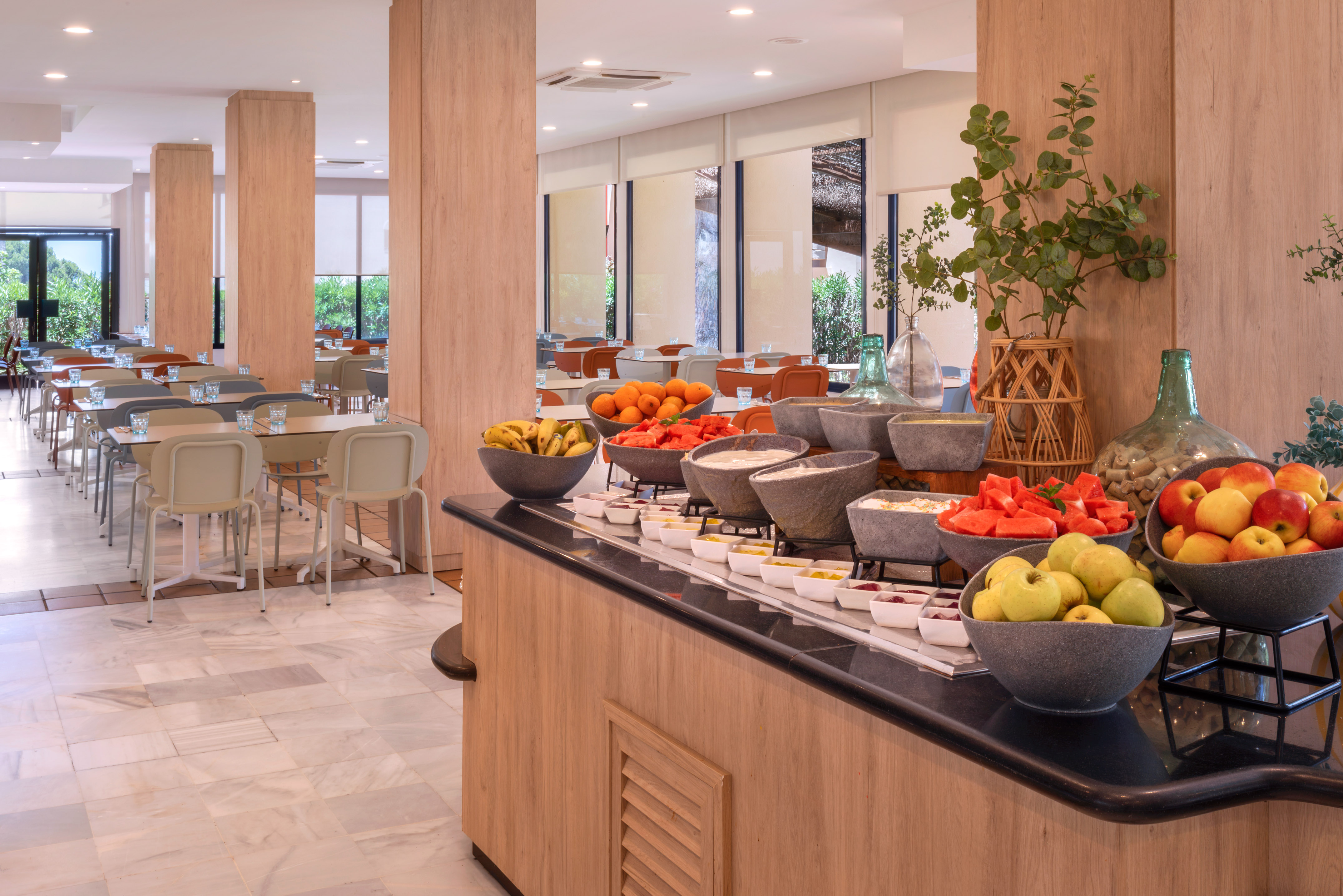 Hotel restaurant breakfast buffet with fresh fruit and dining tables.