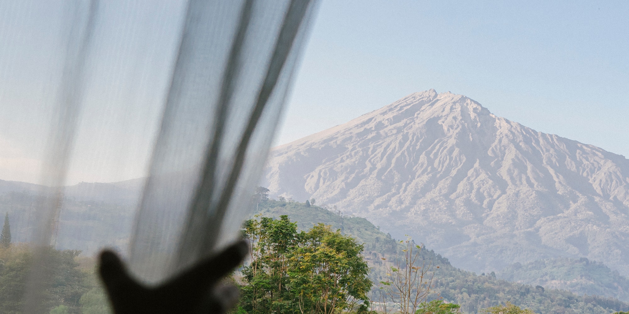 a person's hand reaching out to a window with a mountain in the background