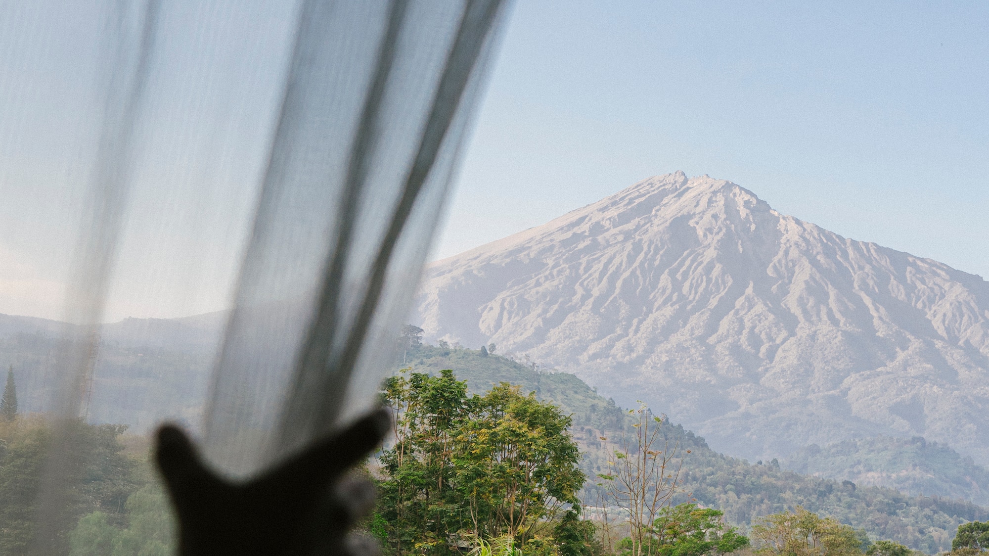 a person's hand reaching out to a window with a mountain in the background