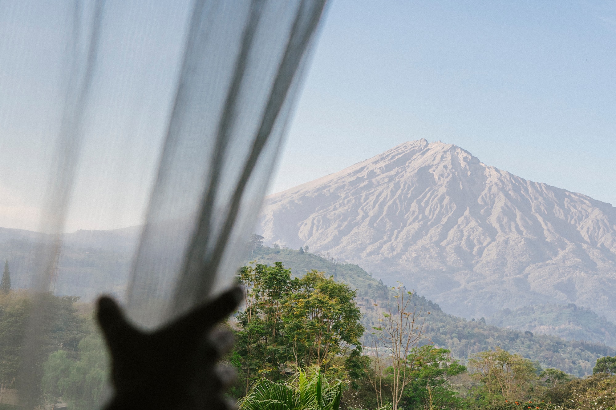 a person's hand reaching out to a window with a mountain in the background