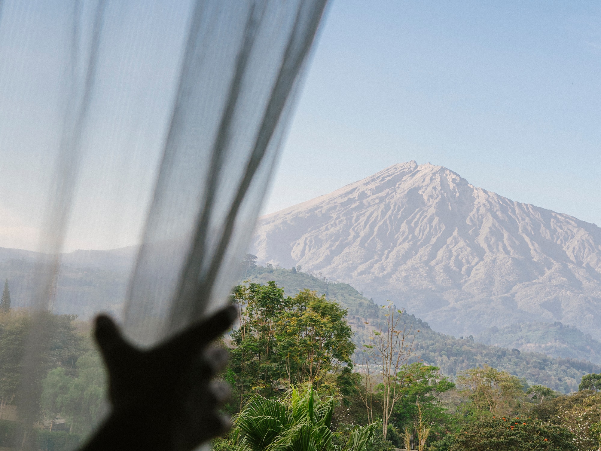 a person's hand reaching out to a window with a mountain in the background