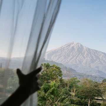 a person's hand reaching out to a window with a mountain in the background