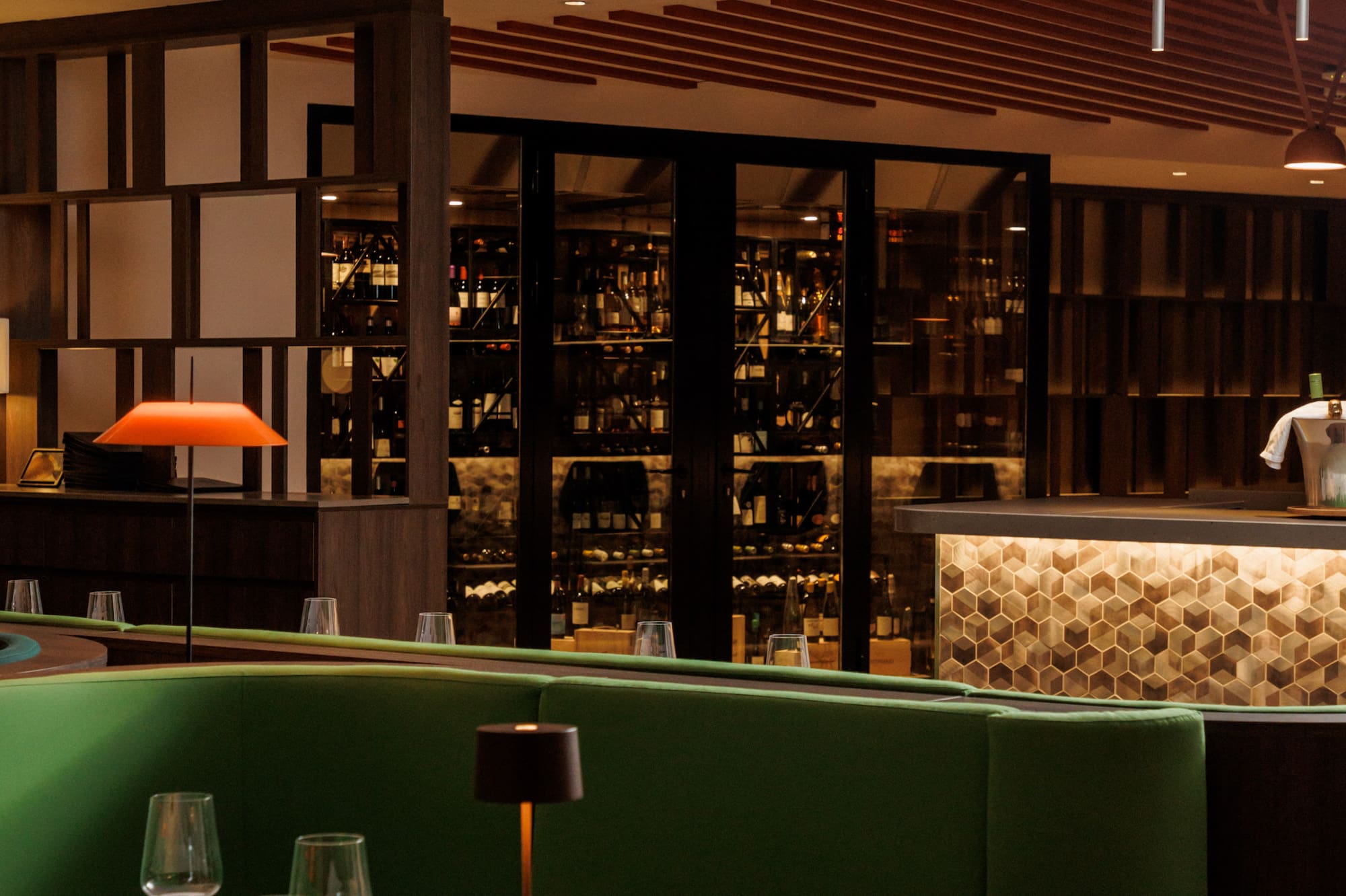 Modern restaurant interior: green booth, set table, wine cellar, illuminated bar.