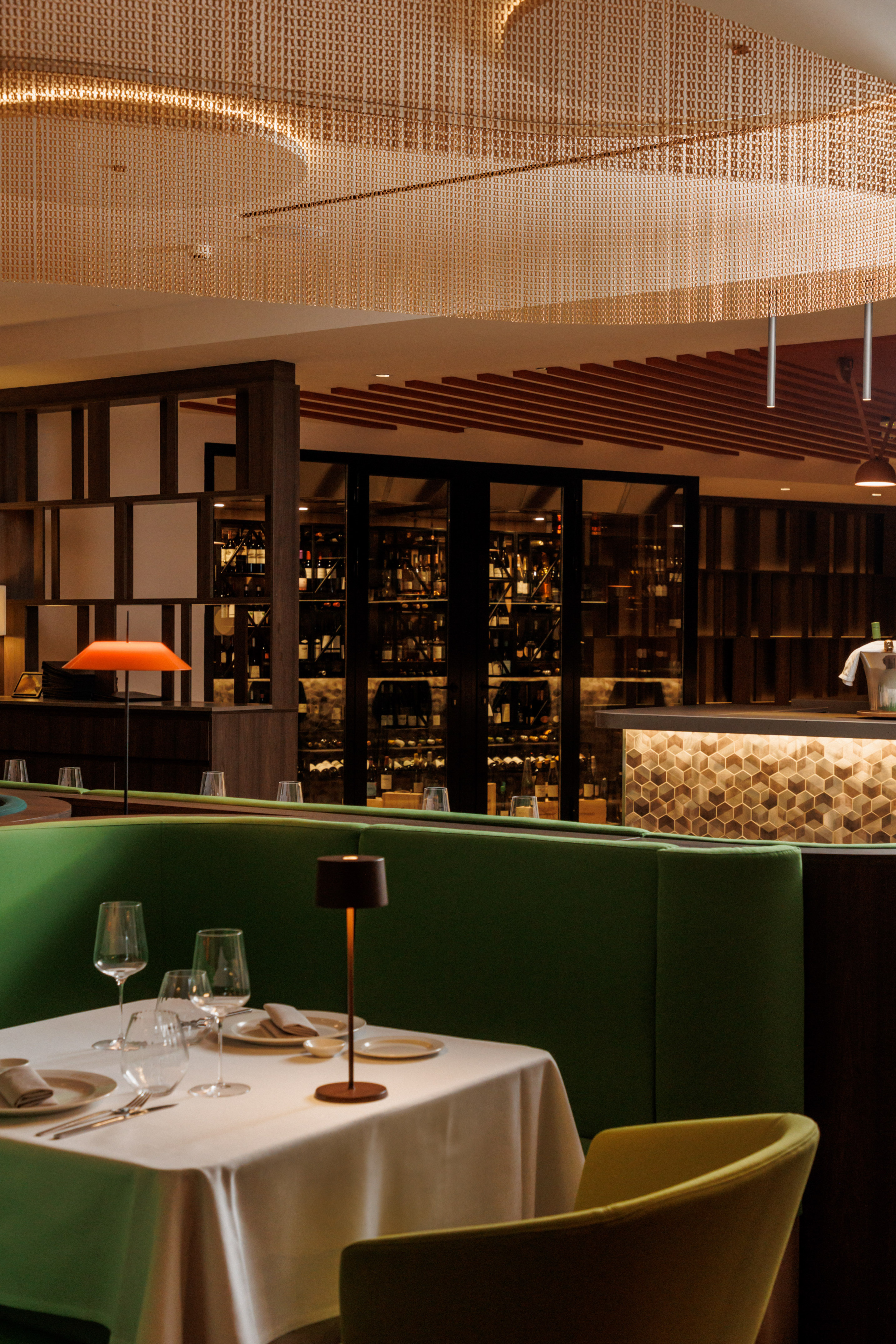 Modern restaurant interior: green booth, set table, wine cellar, illuminated bar.
