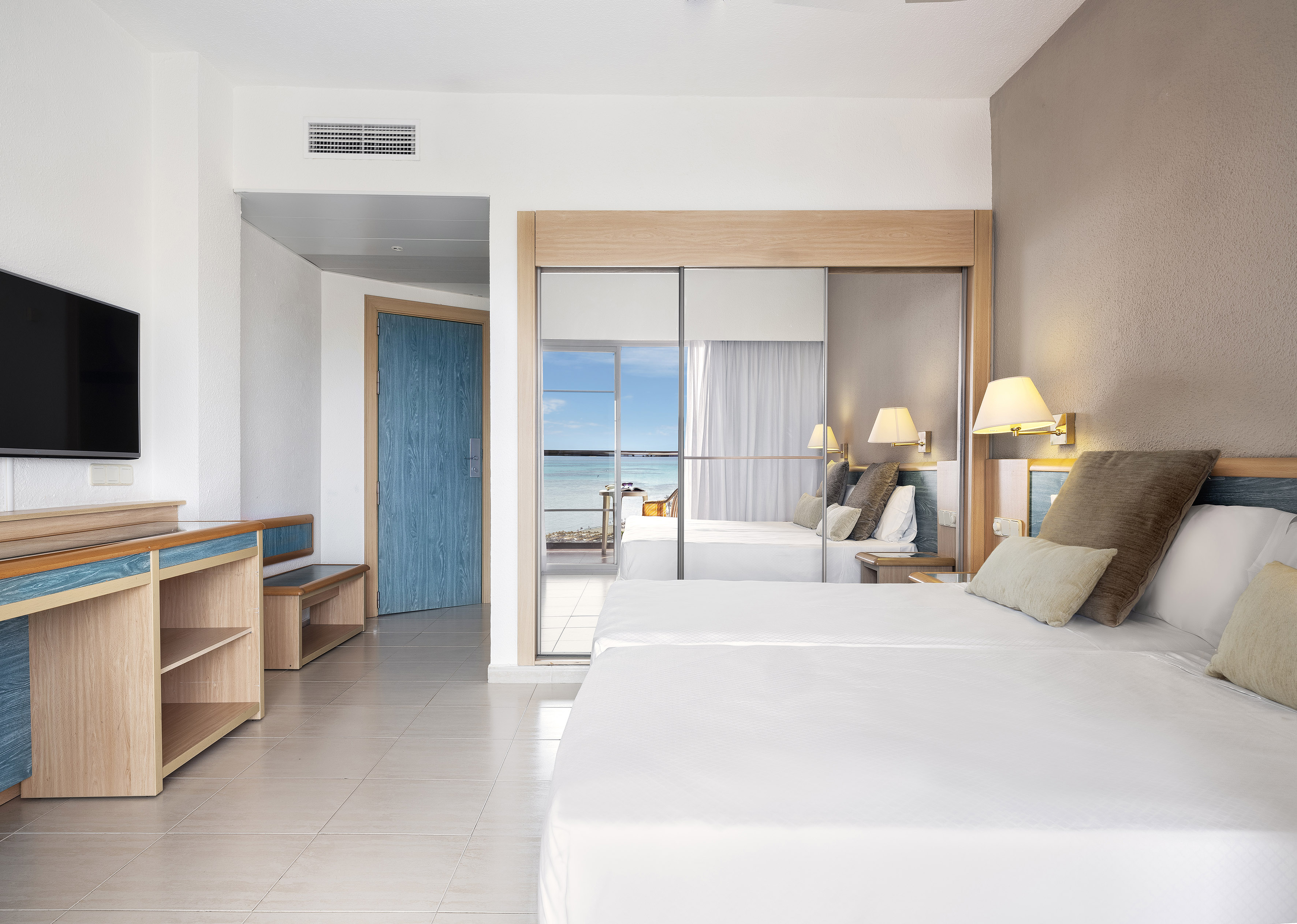 Ocean view hotel room with twin beds, blue furniture, and mirrored wardrobe.
