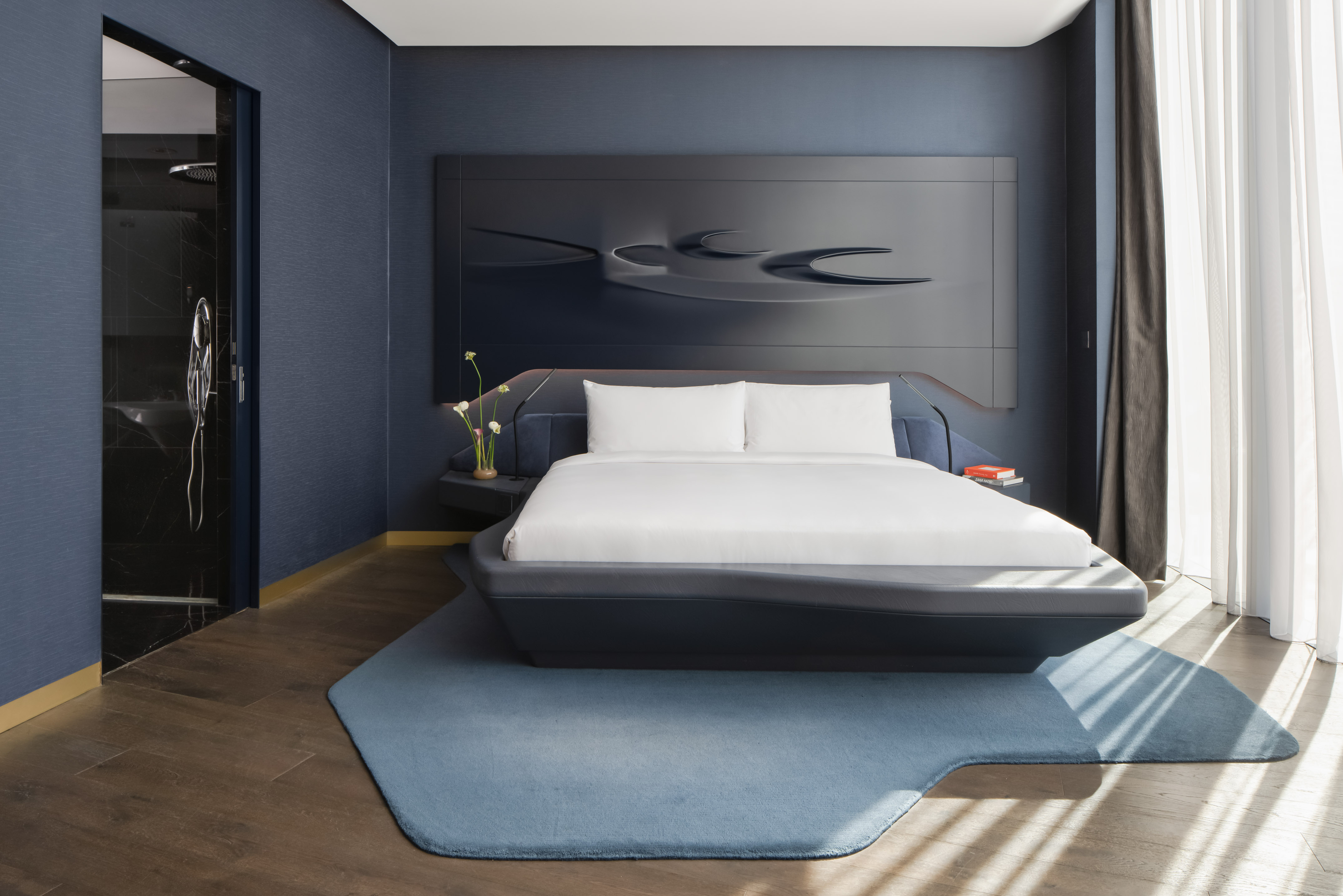 Modern dark blue bedroom with contemporary bed, abstract headboard, and wood floor.