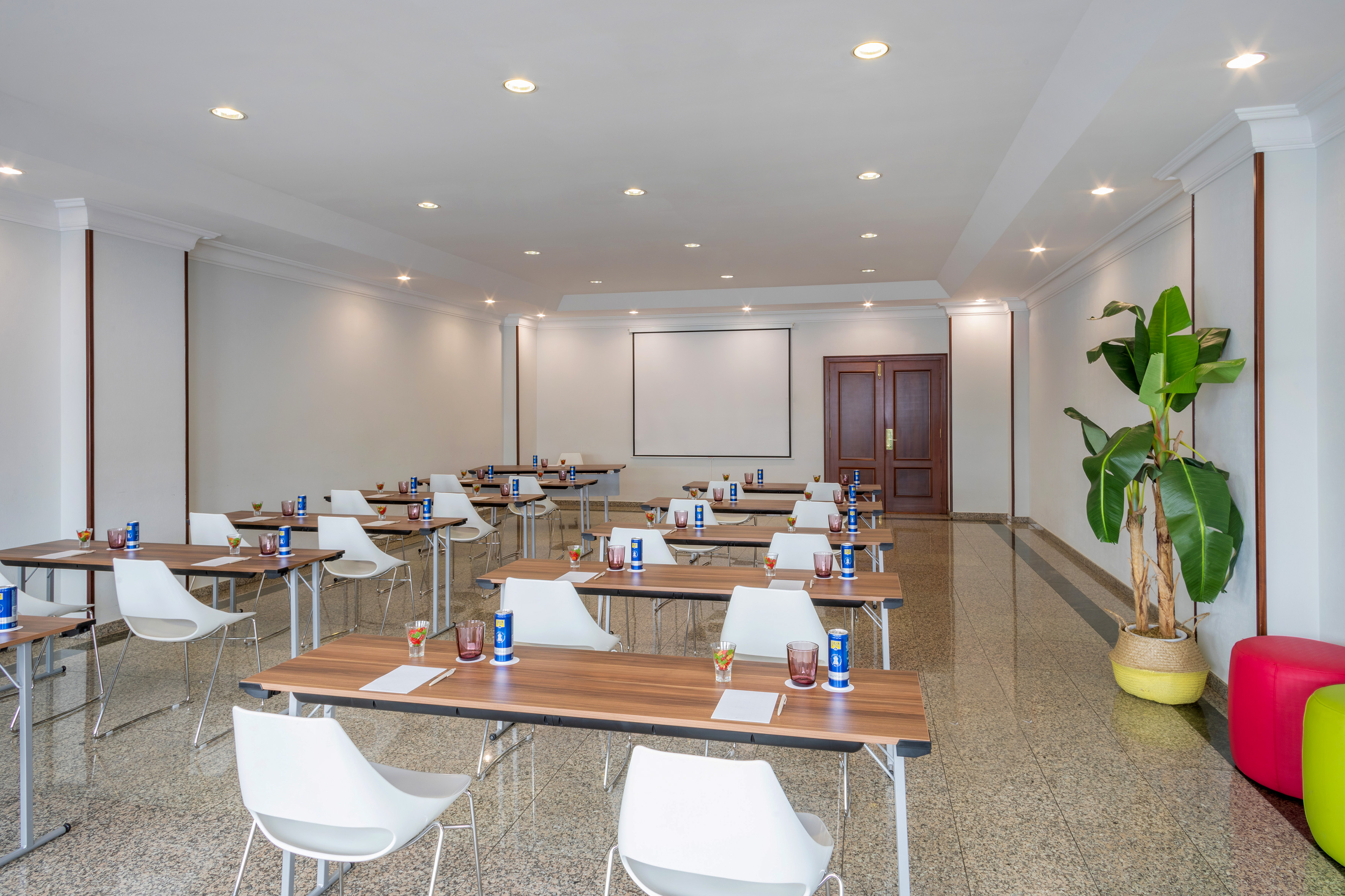 Bright training room setup with tables, white chairs, and a projector screen.