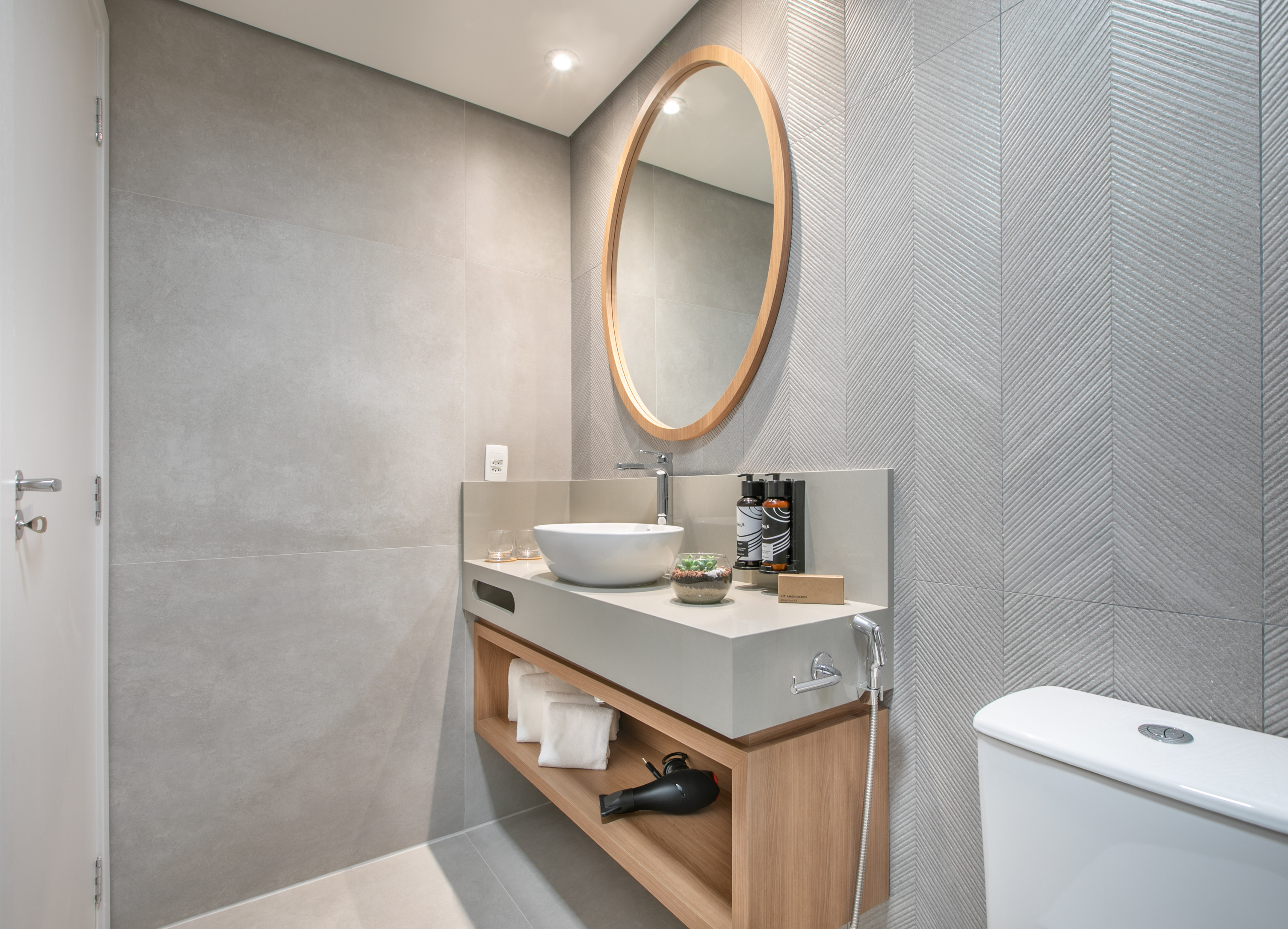Modern bathroom with grey chevron tiles, wood vanity, vessel sink, and oval mirror.