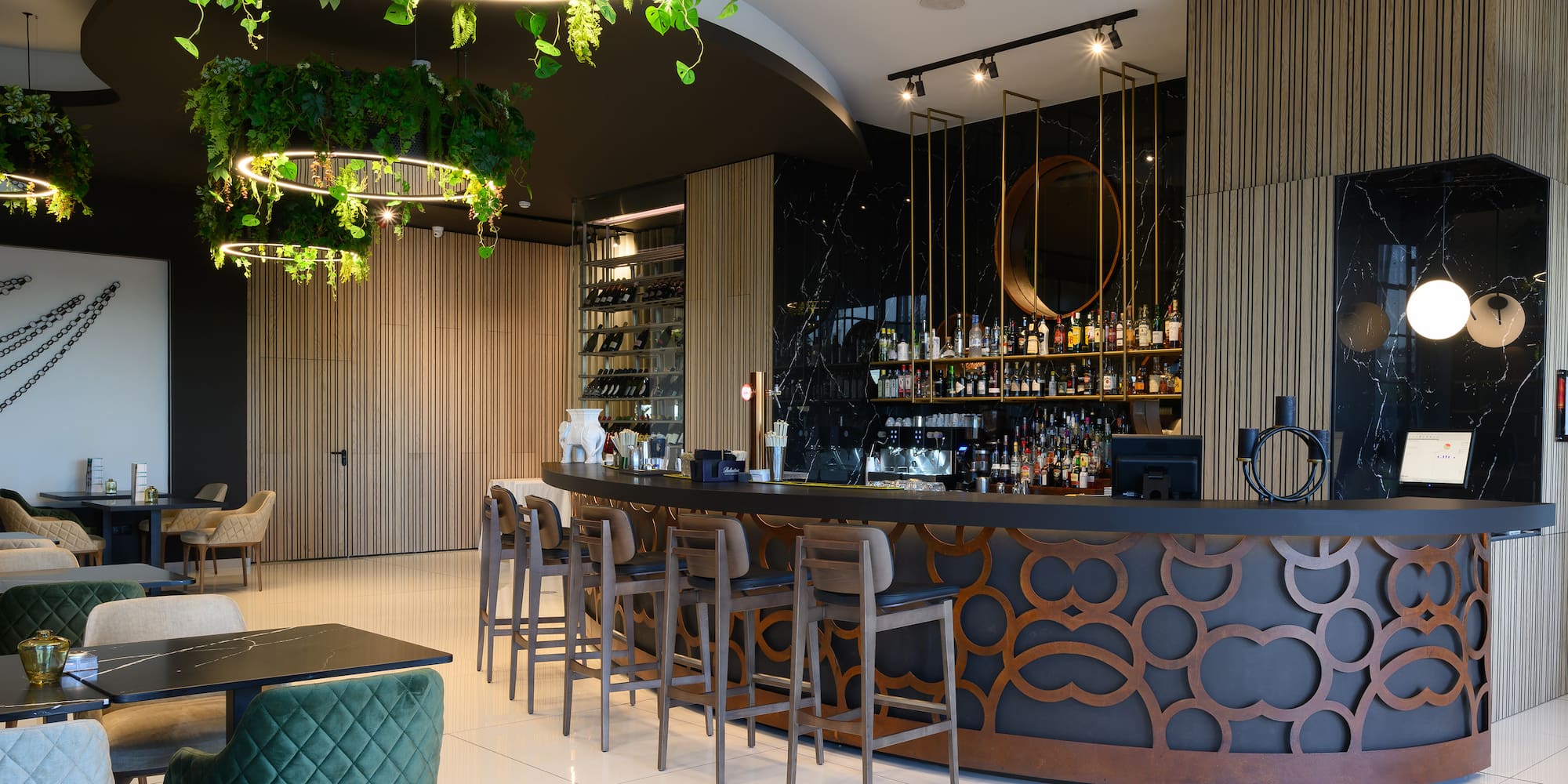 a bar with a long counter and chairs in a room with plants from the ceiling