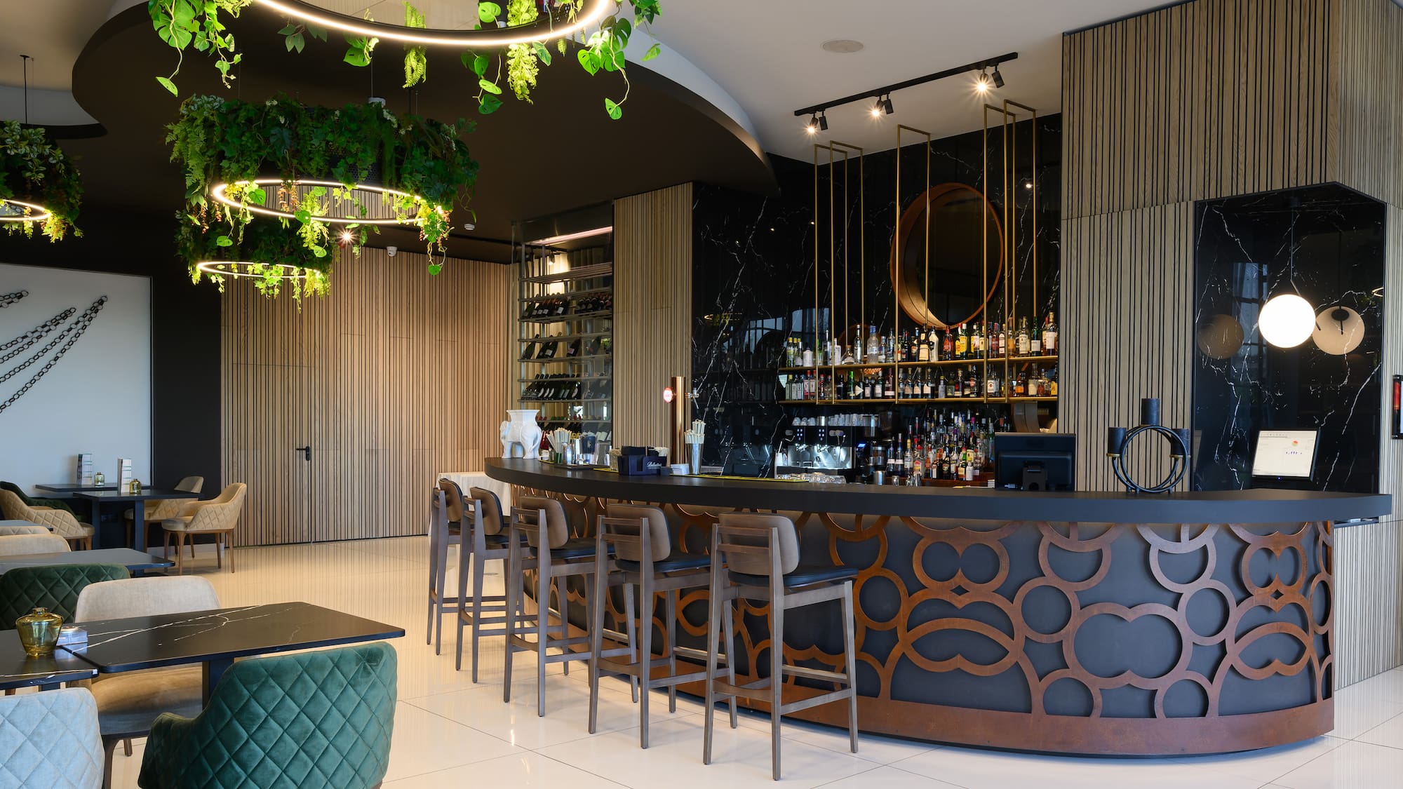 a bar with a long counter and chairs in a room with plants from the ceiling