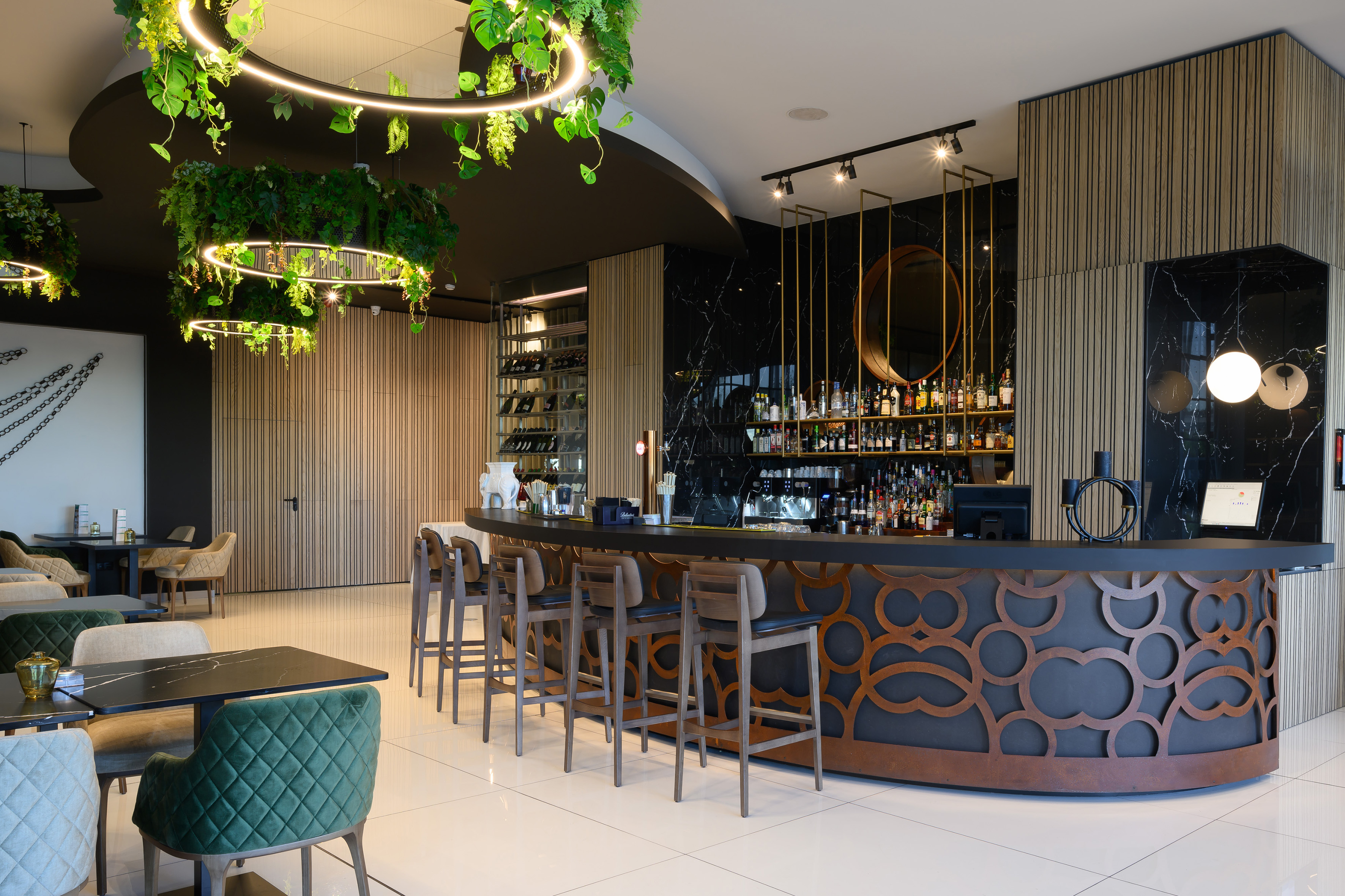 a bar with a long counter and chairs in a room with plants from the ceiling