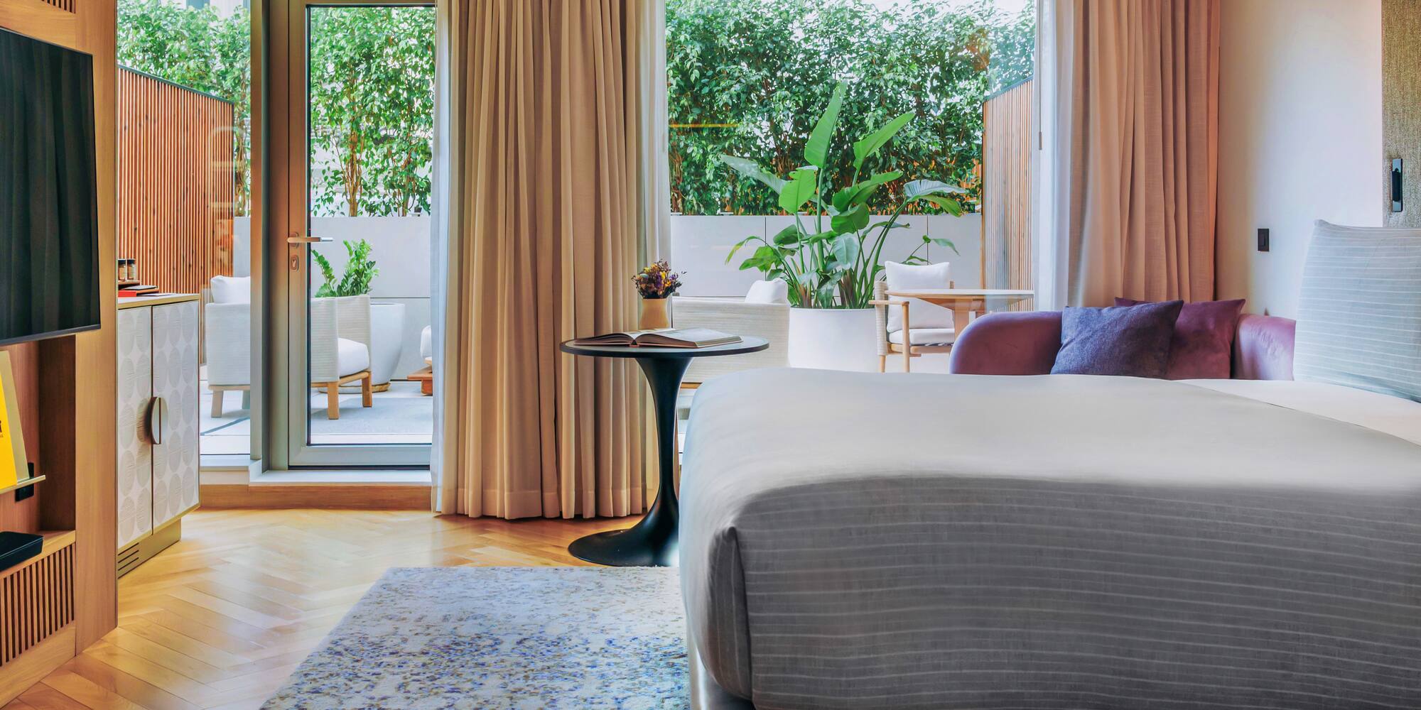 Modern hotel room with bed, private patio, lush greenery, and stylish decor.