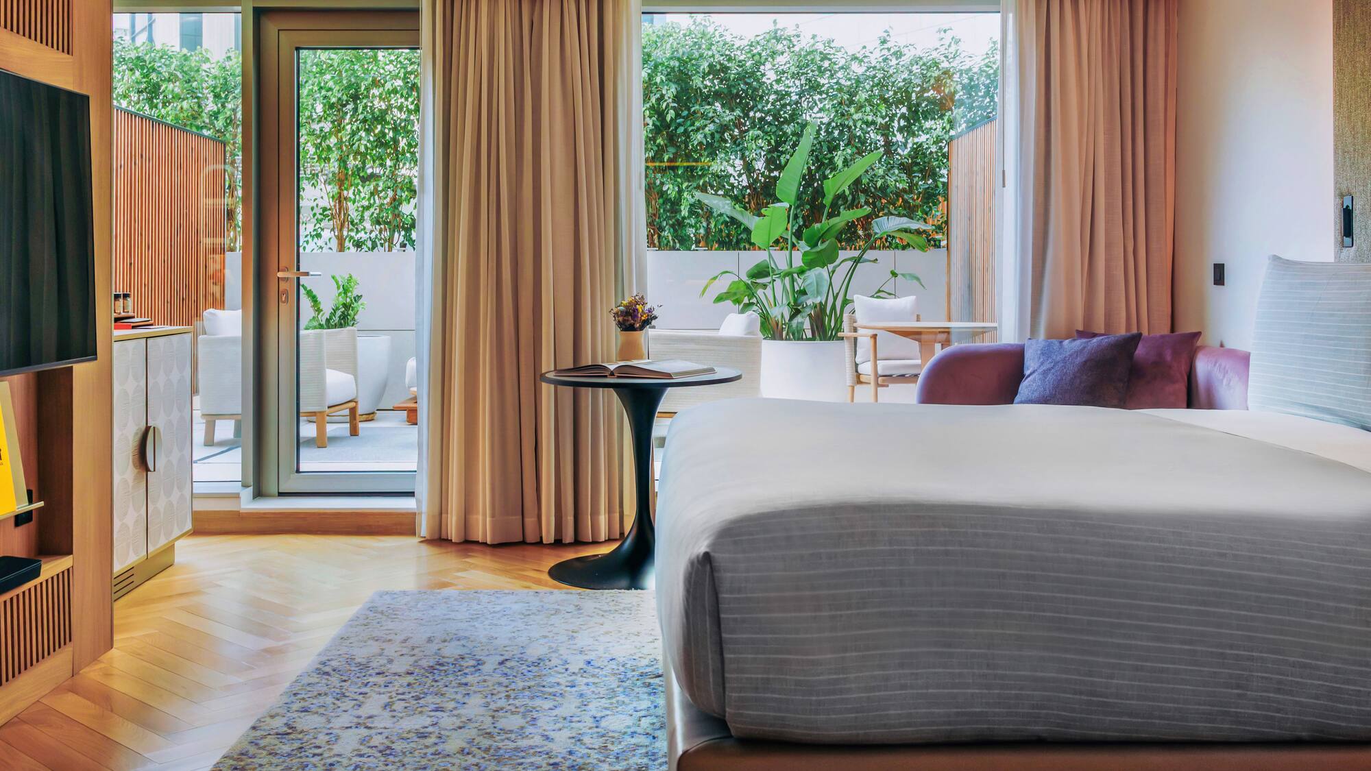Modern hotel room with bed, private patio, lush greenery, and stylish decor.