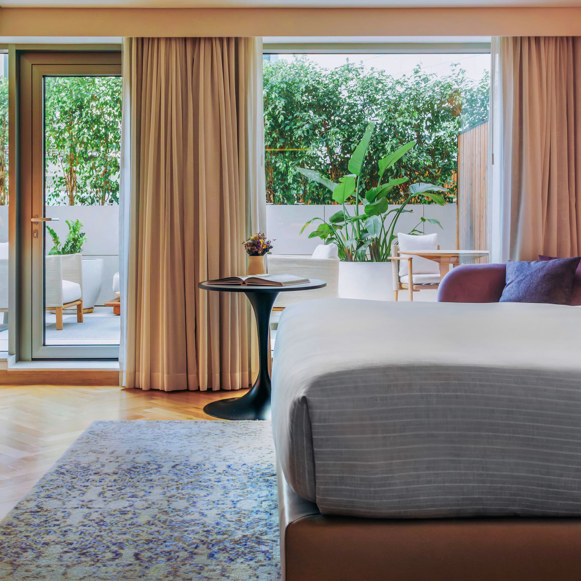 Modern hotel room with bed, private patio, lush greenery, and stylish decor.
