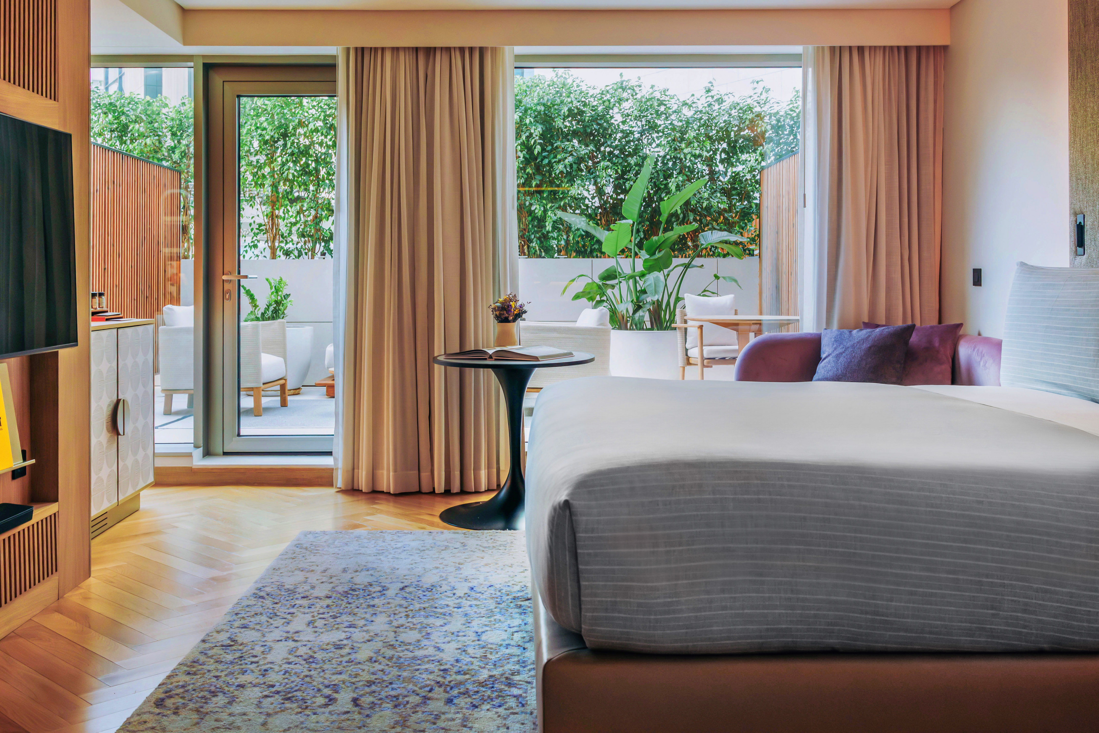 Modern hotel room with bed, private patio, lush greenery, and stylish decor.