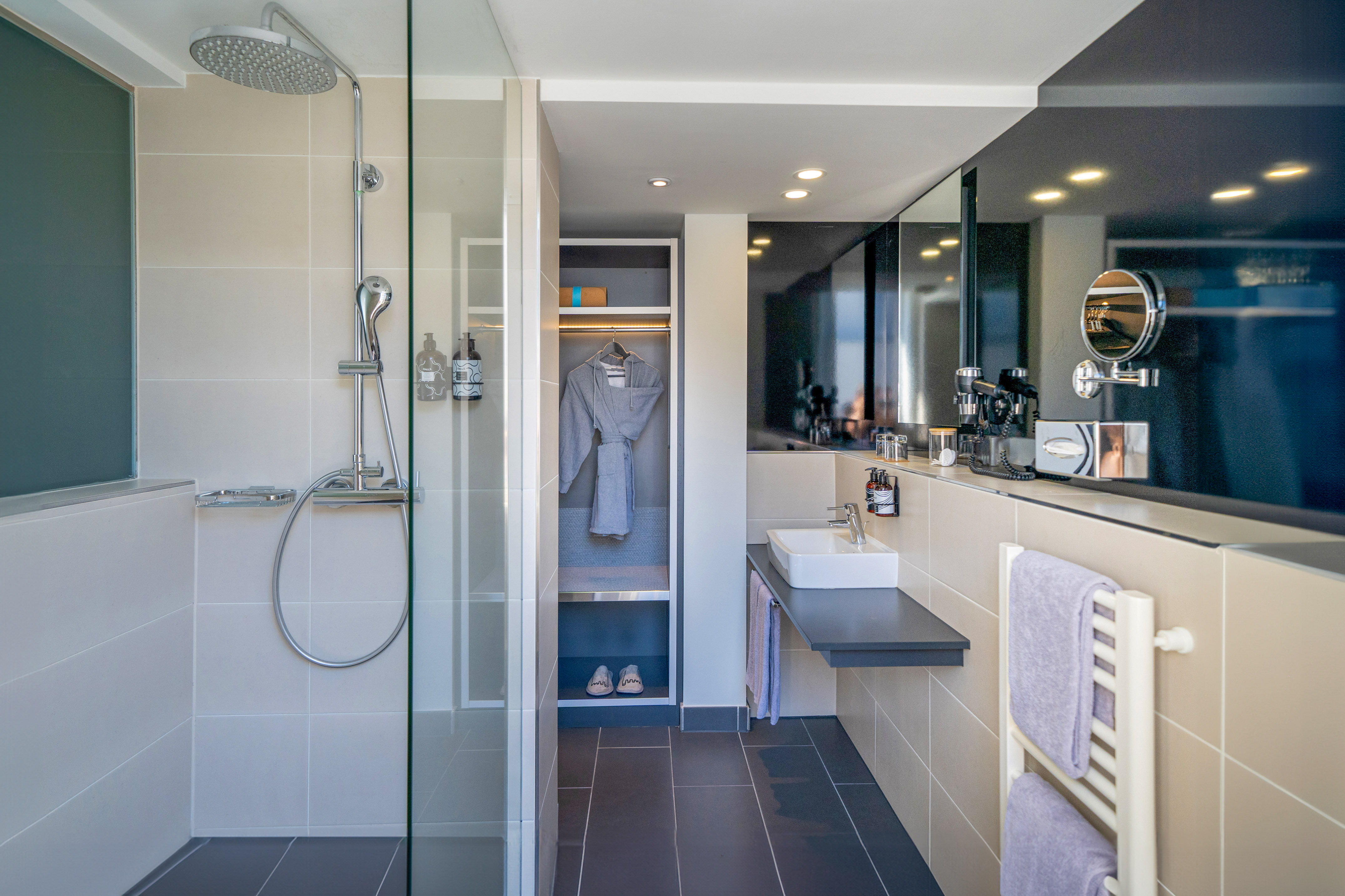 Modern bathroom with glass shower, sleek vanity, and grey bathrobe.