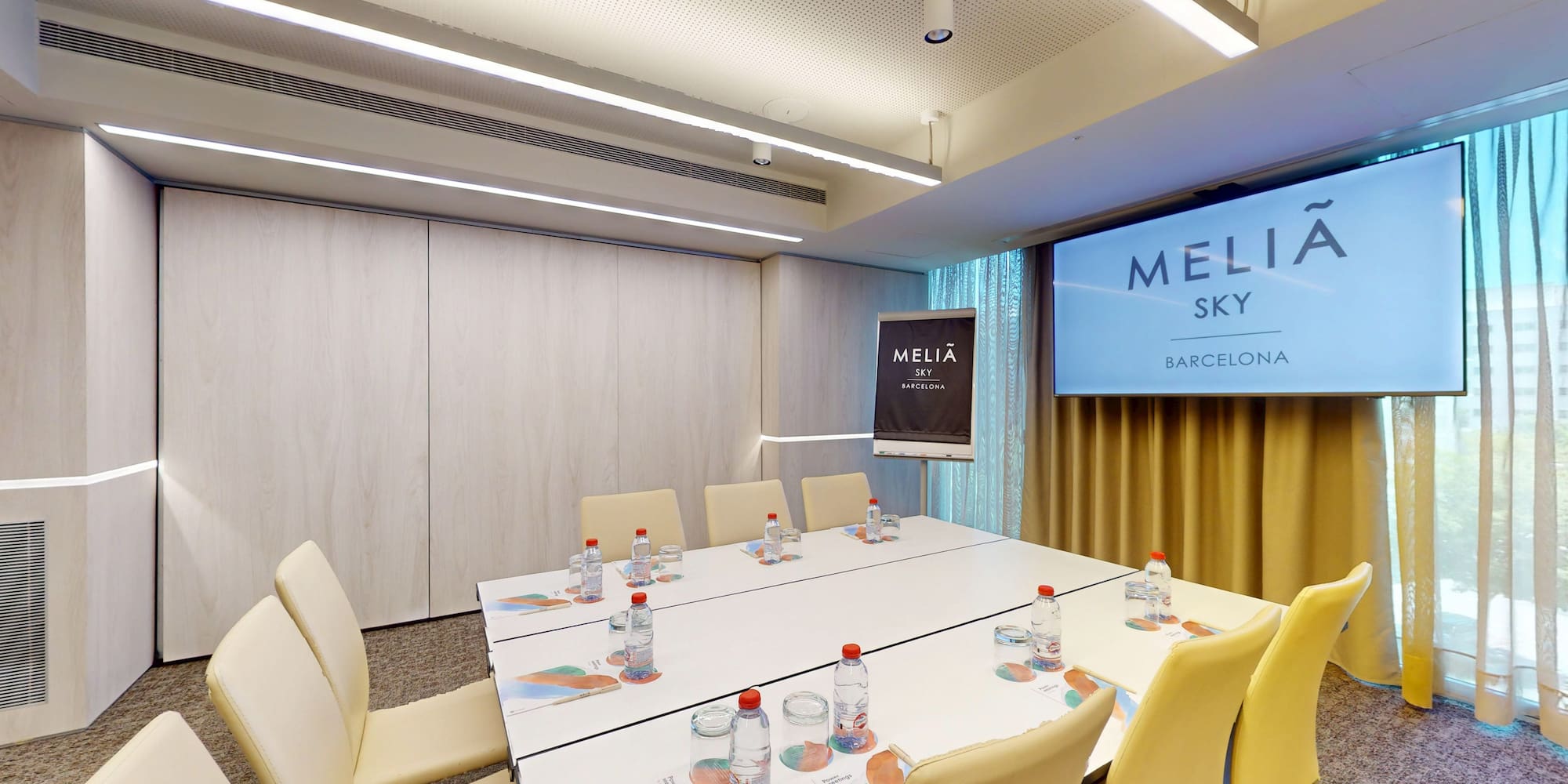Modern Meliá Sky Barcelona meeting room with large table, screen, and flipchart.