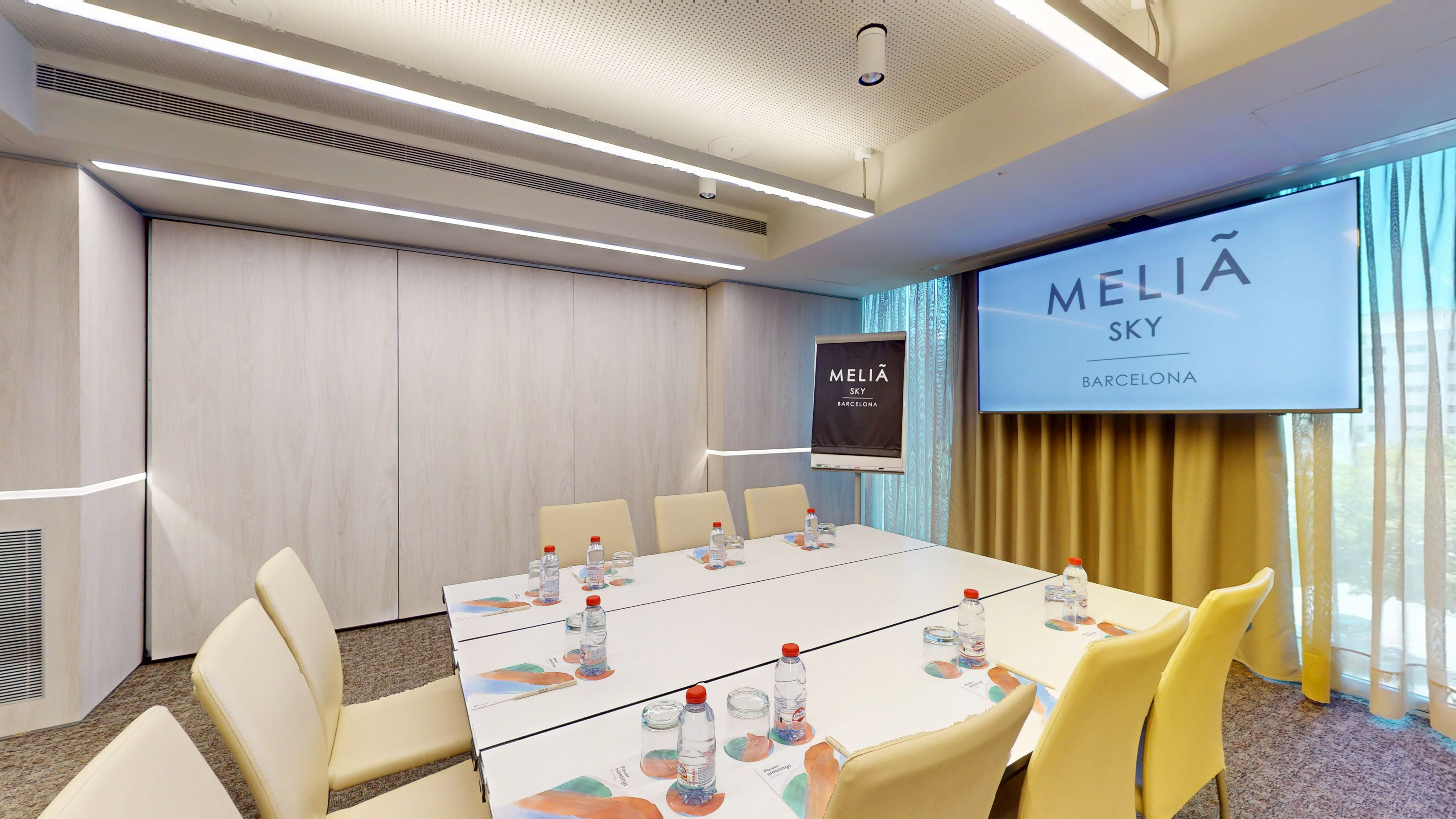 Modern Meliá Sky Barcelona meeting room with large table, screen, and flipchart.