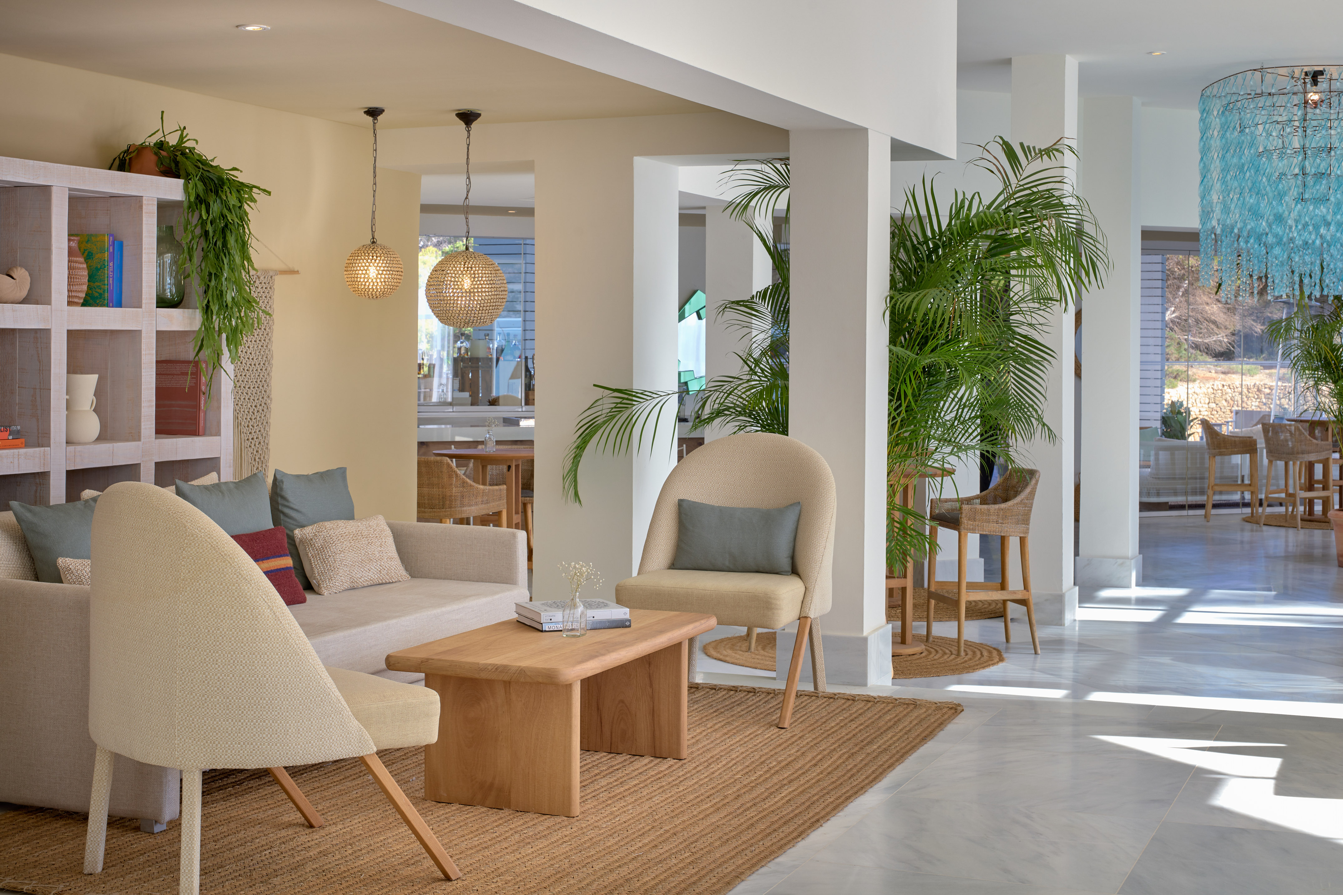 Modern hotel lounge with neutral furniture, palm plants, and natural light.