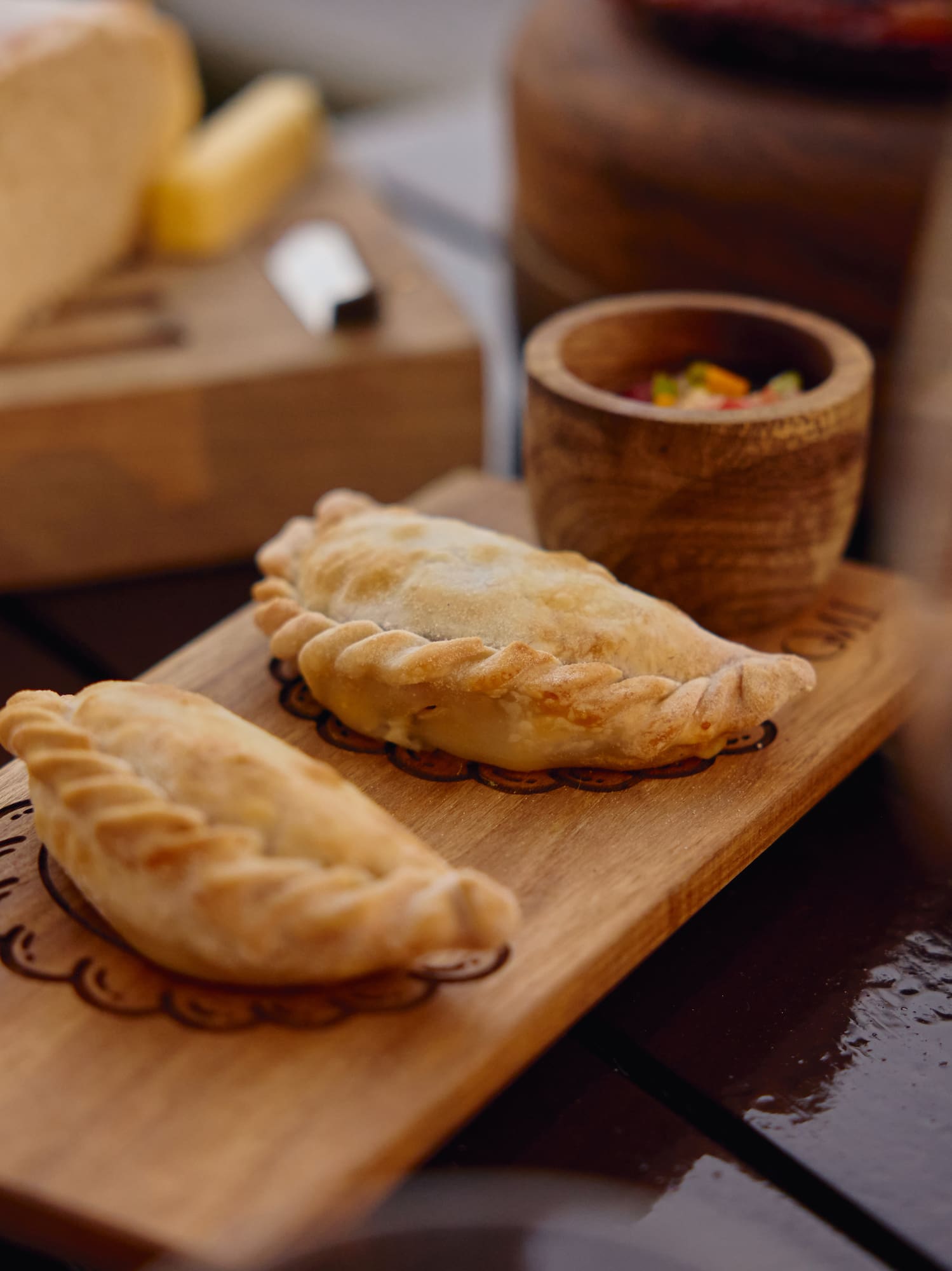Empanadas doradas sobre tabla de madera, con salsa, queso y vino.