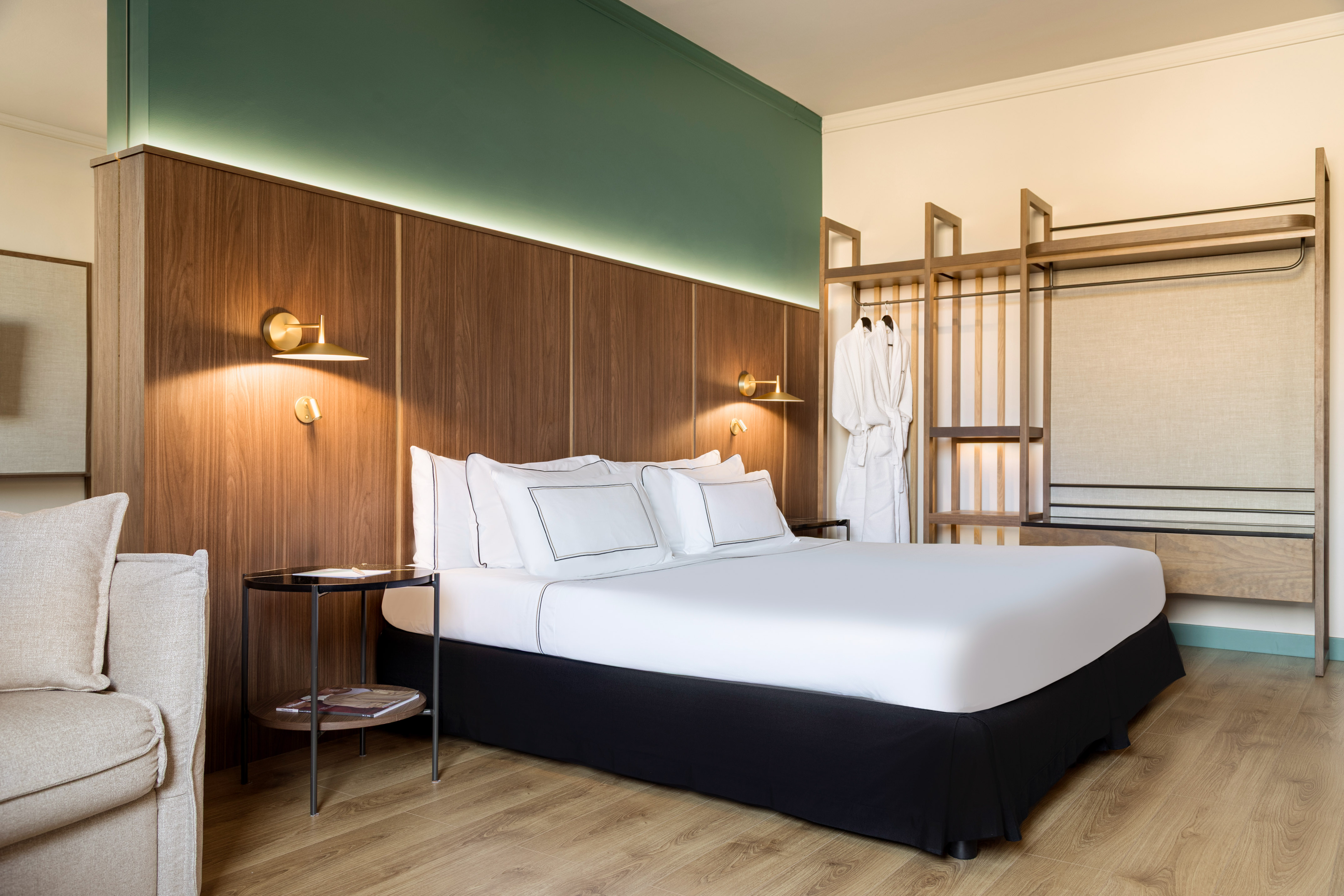 Modern hotel room with wood headboard, white bed, green wall, and open wardrobe.