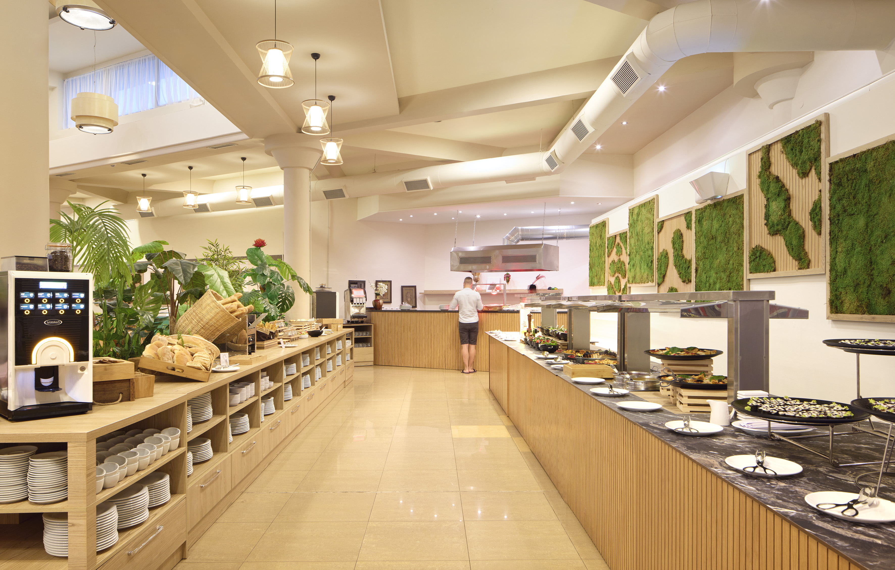 Modern hotel buffet with self-service food, beverage dispenser, and plant decor.