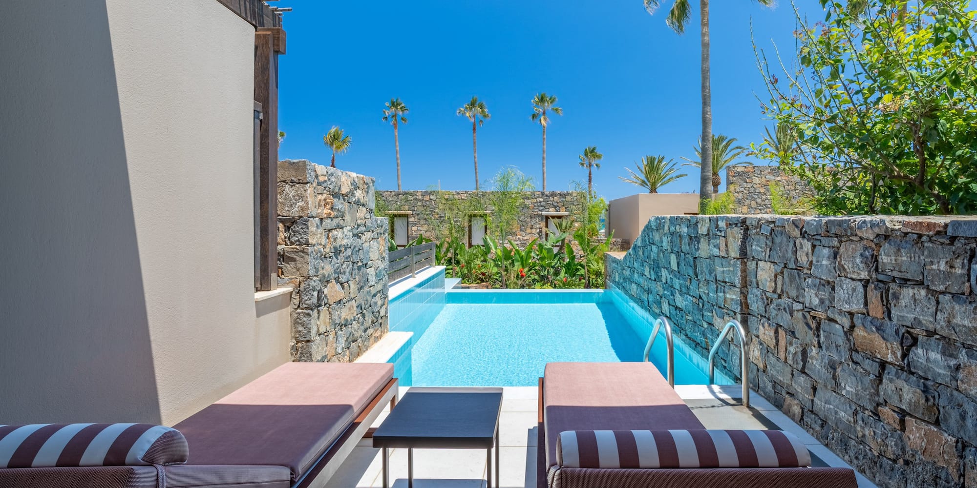 Resort private pool with sun loungers, stone walls, and palm trees.