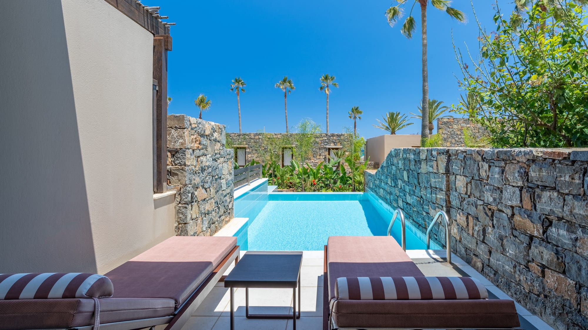 Resort private pool with sun loungers, stone walls, and palm trees.