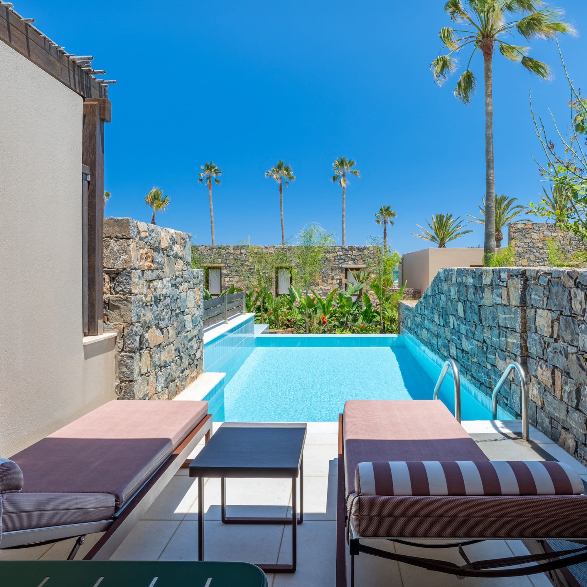 Resort private pool with sun loungers, stone walls, and palm trees.